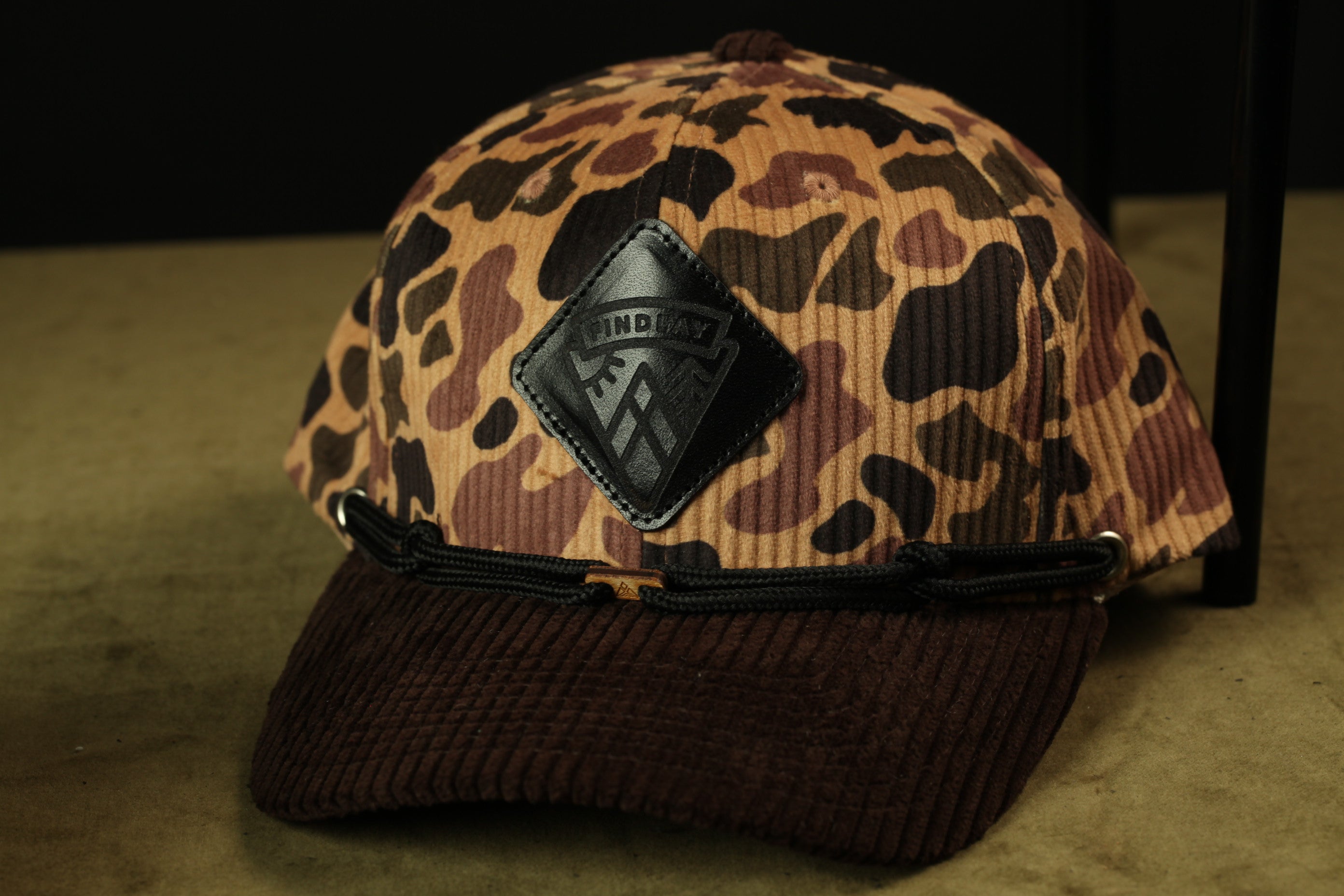 A camouflage-patterned baseball cap with a black leather patch on the front.