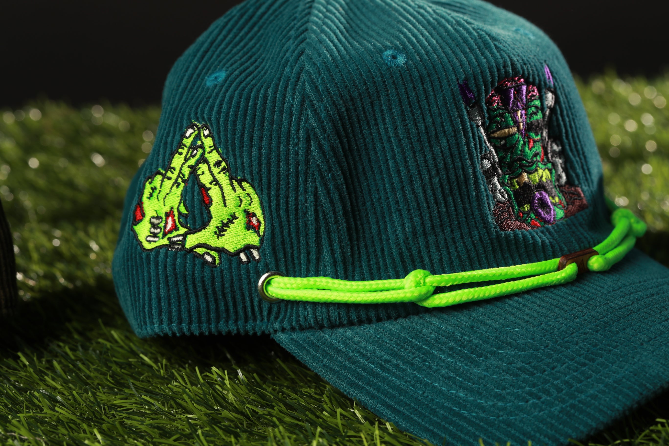 A close-up image of a green baseball cap with a unique design featuring a green monster or creature on the front.