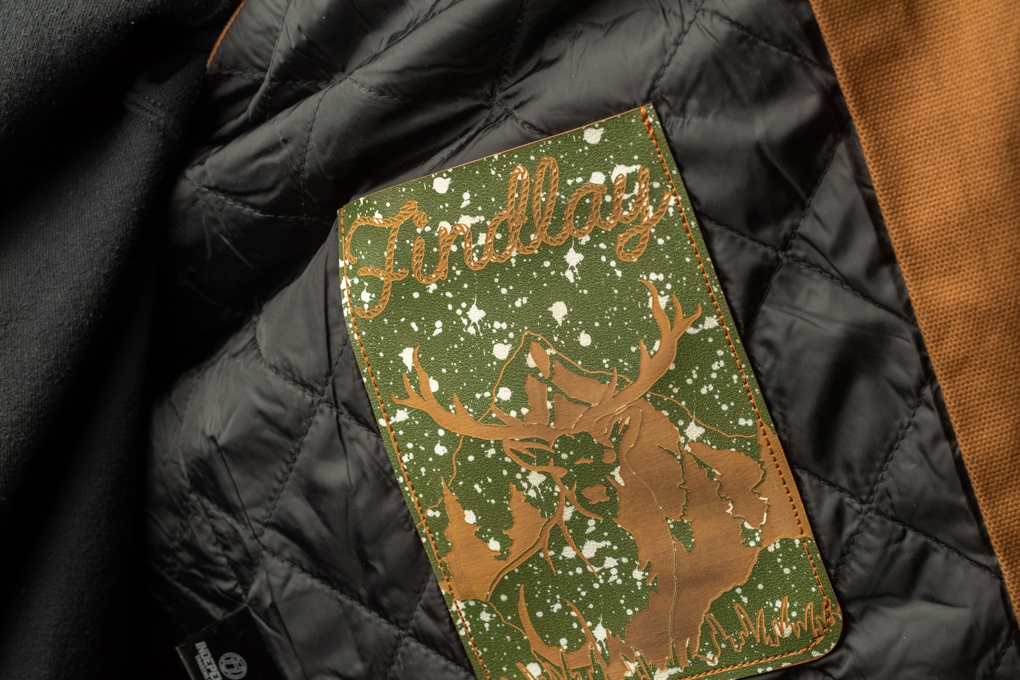 A close-up view of a green and gold patch with a deer silhouette and snowflakes on a black quilted fabric.