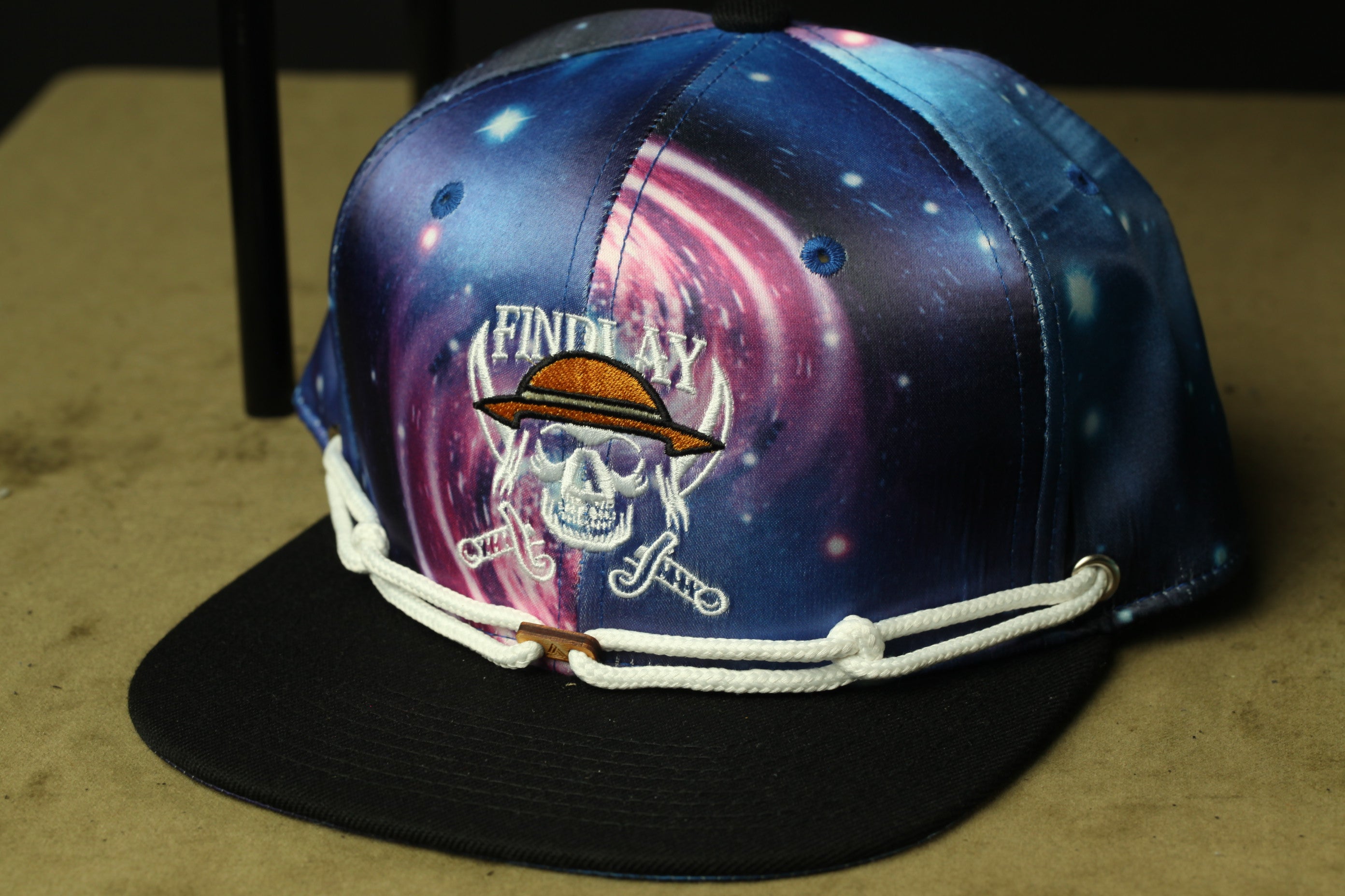 A colorful baseball cap with a skull and crossbones design, featuring the text "FIND AY" on the front.