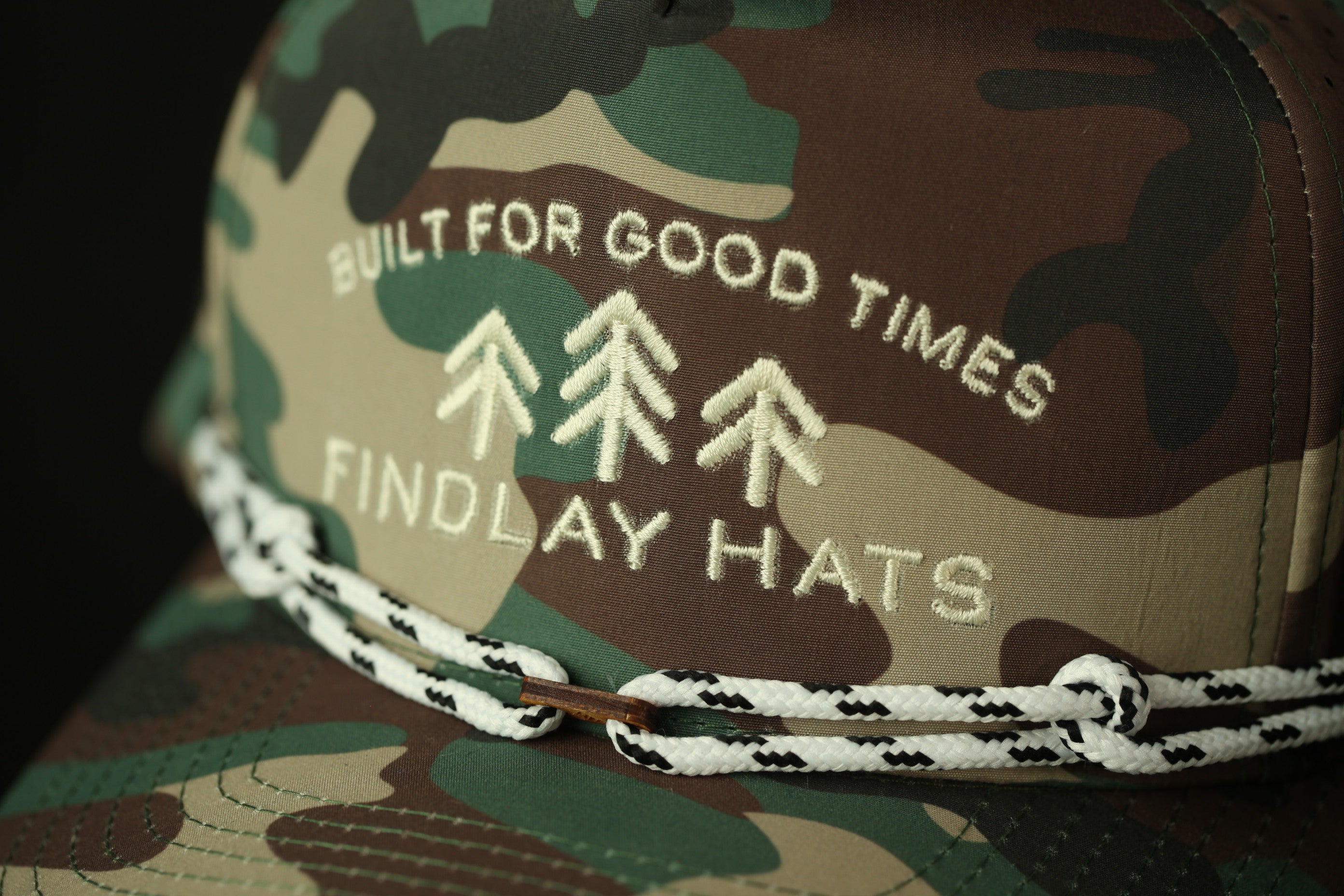 A close-up of a camouflage hat with the text "BUILT FOR GOOD TIMES FINDLAY HATS" embroidered on it.