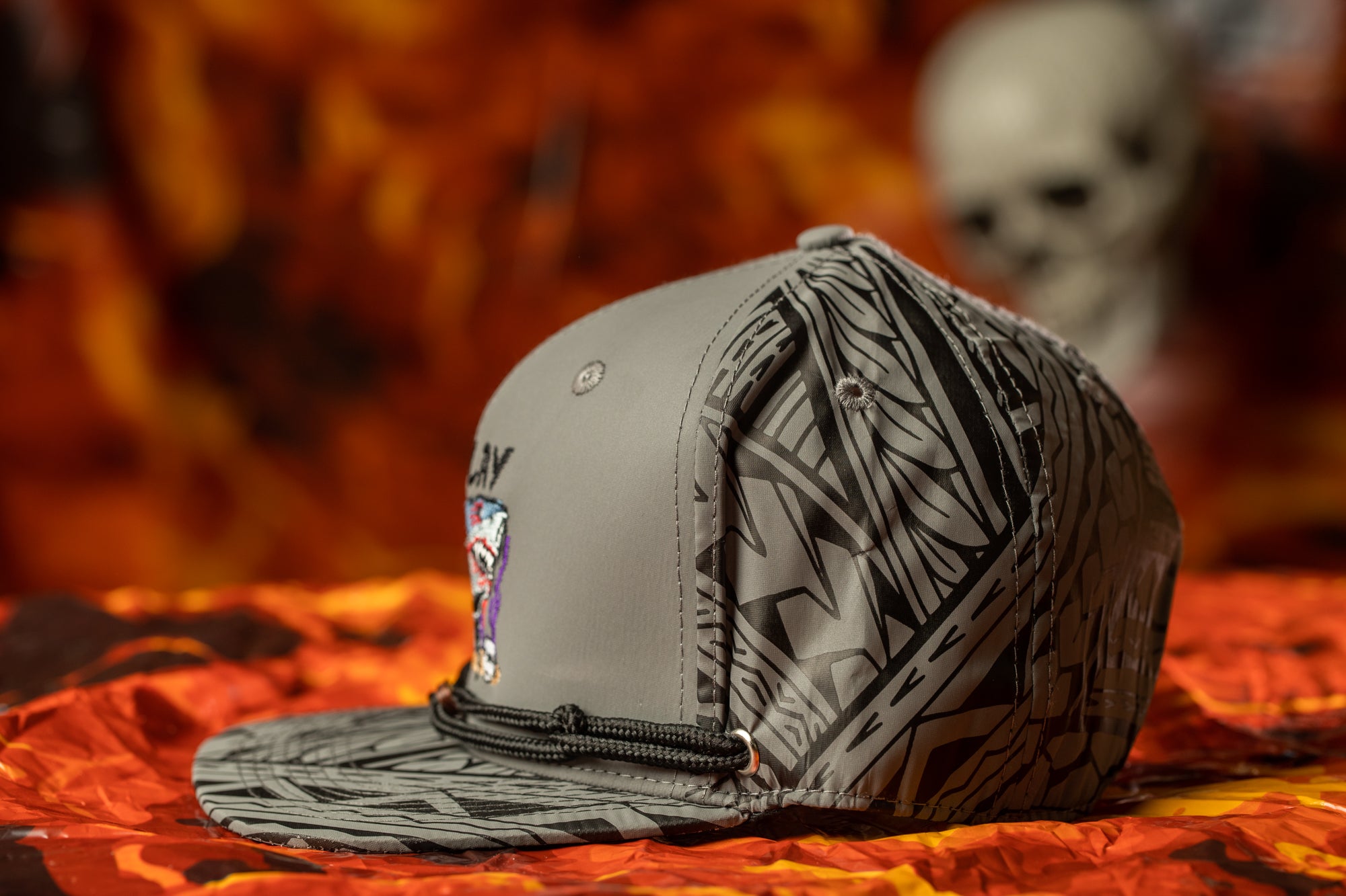 A gray baseball cap with a black and white geometric pattern is displayed on a red and orange background.