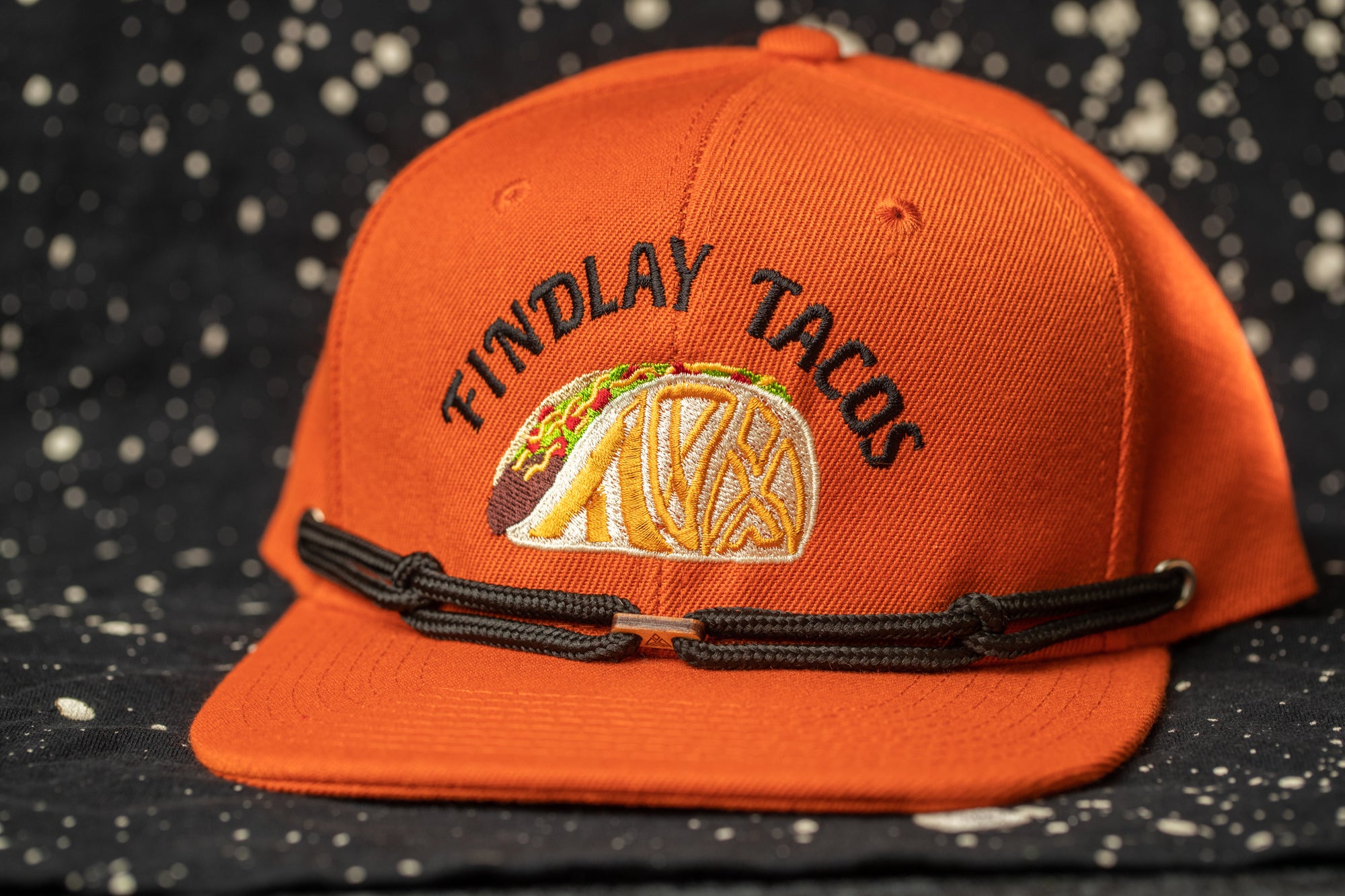An orange baseball cap with a black strap and a graphic of a taco on the front.