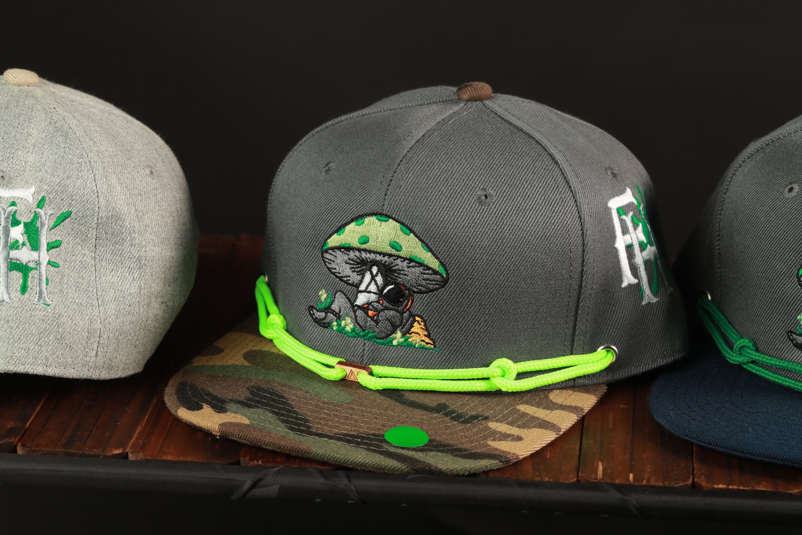 Three baseball caps are displayed on a wooden surface, each with unique designs and colors.