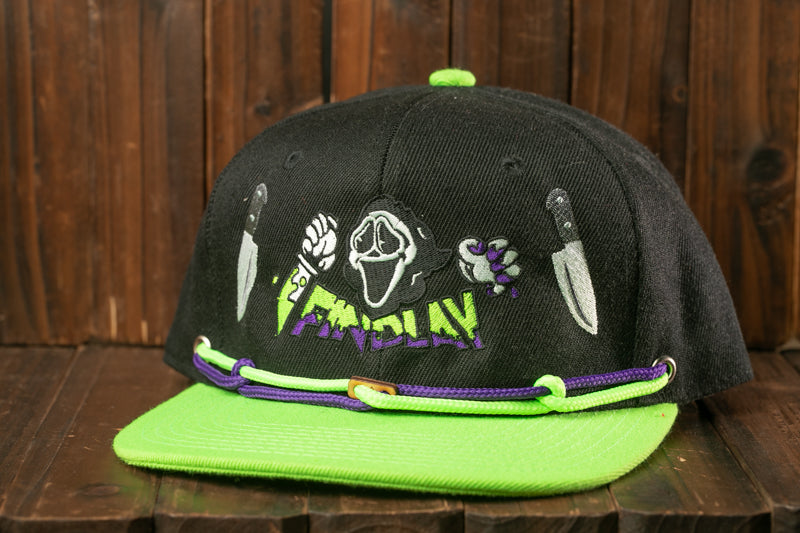 A black baseball cap with a green brim and purple accents, featuring a graphic design with a skull and crossbones symbol, a knife, and the word "FRIDAY" printed on it.