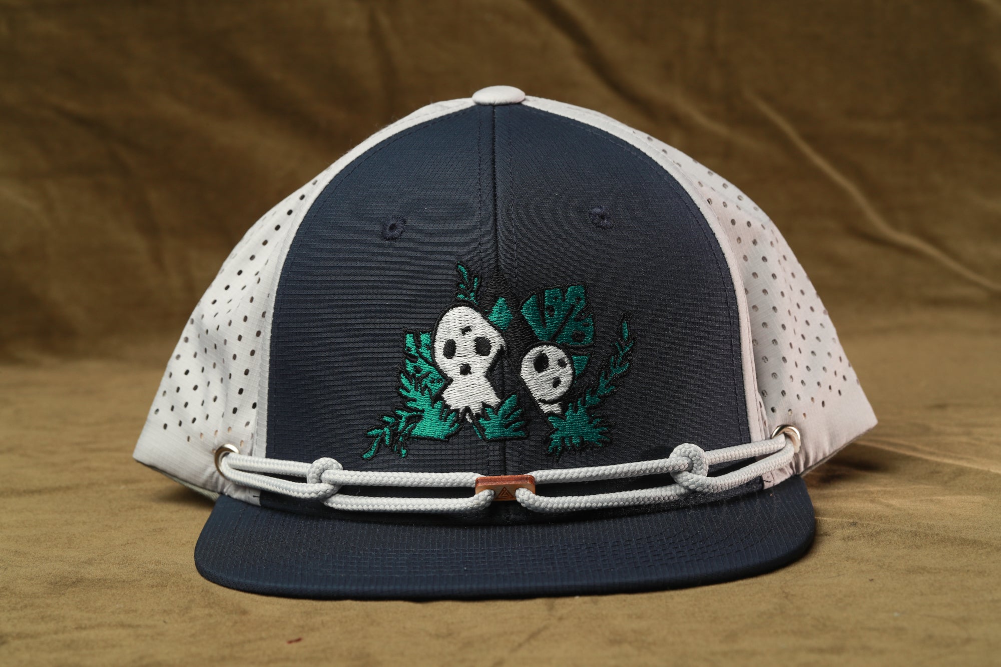 A navy blue baseball cap with a white perforated brim and a green skull and crossbones design on the front.