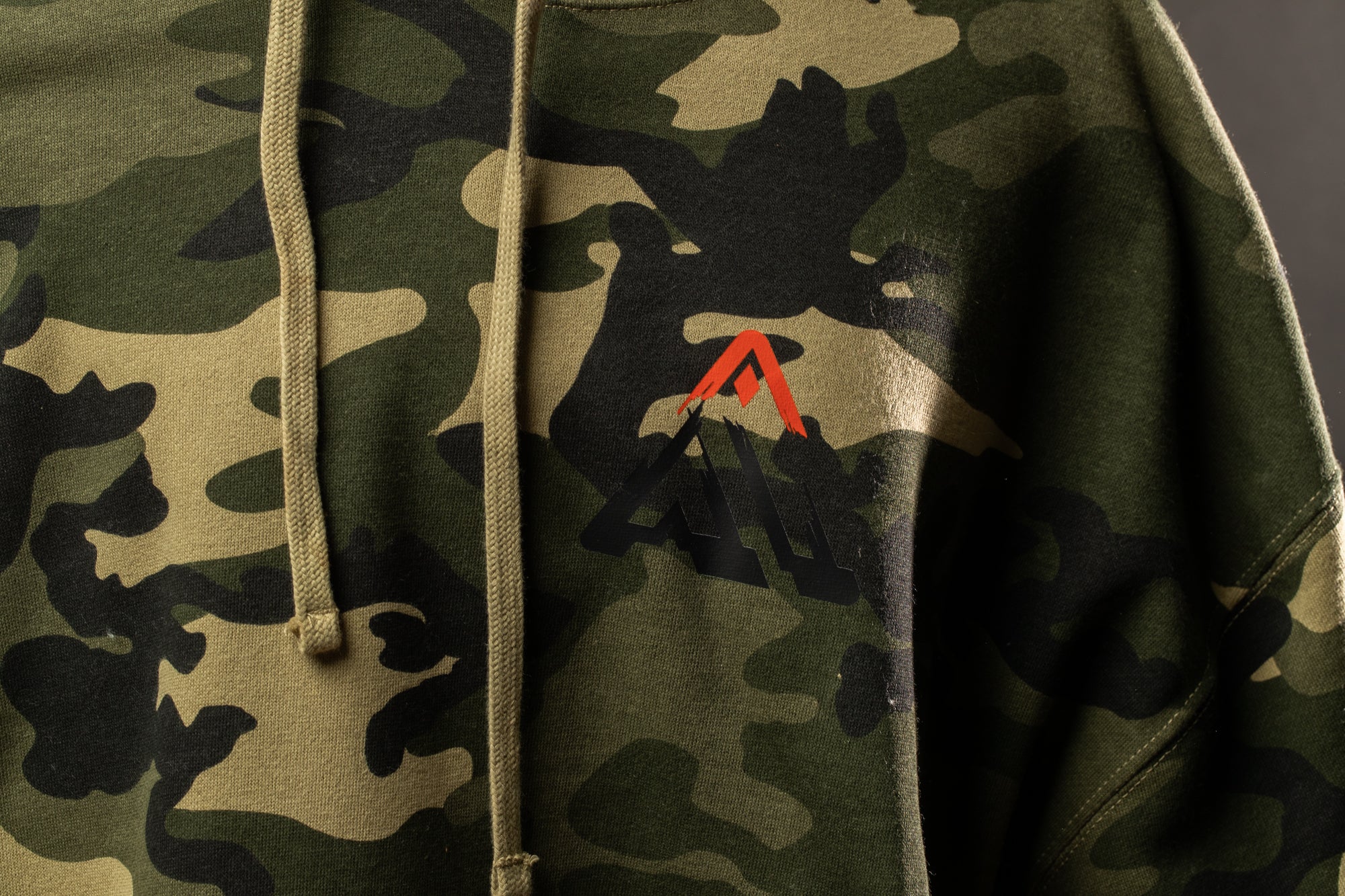 A close-up view of a person wearing a camouflage-patterned hoodie with a red logo on the front.