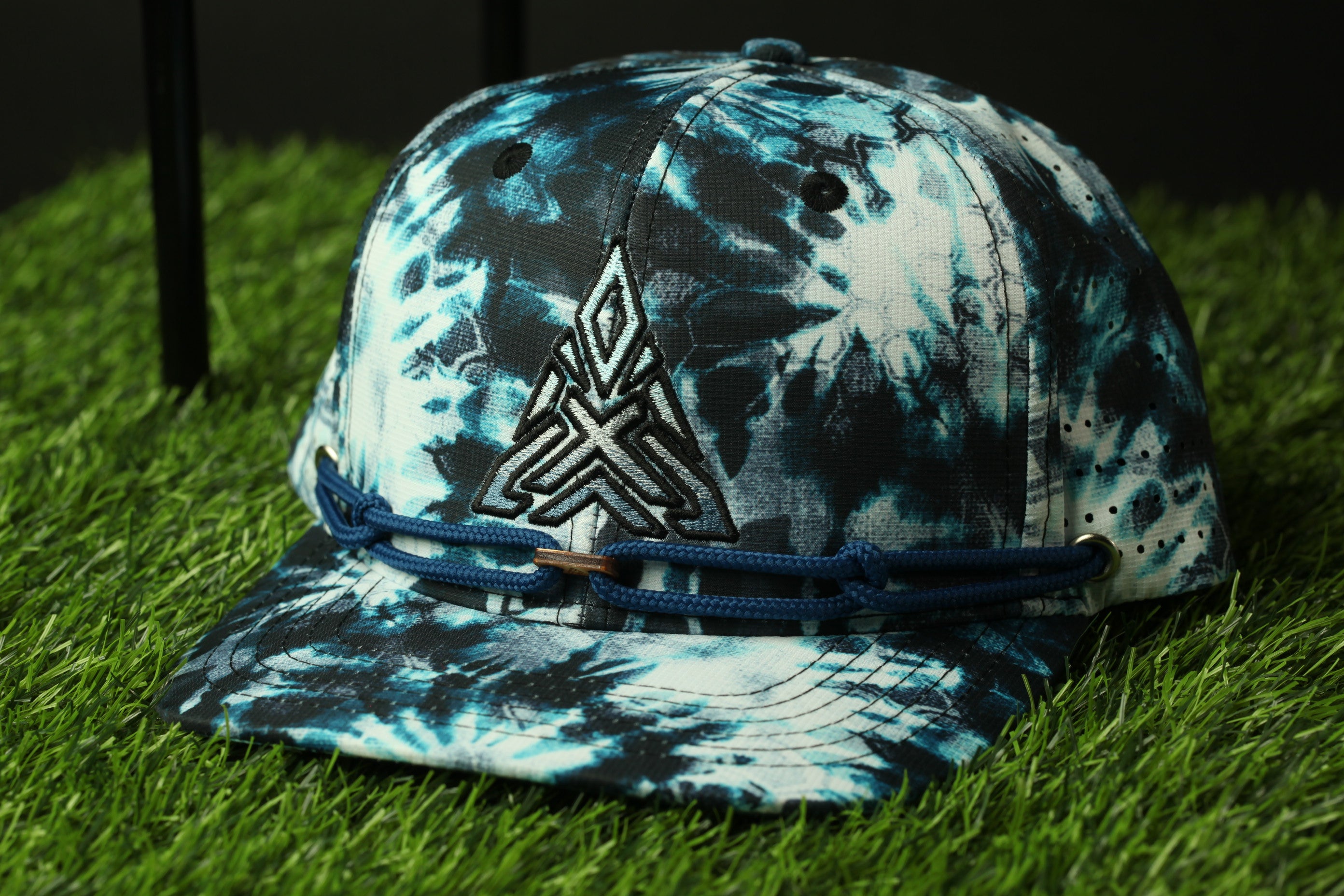 A tie-dye baseball cap with a black and white pattern sits on a grassy surface.
