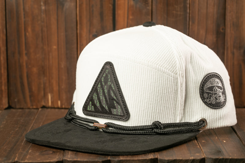 A white baseball cap with a black brim and a triangular patch on the front, placed on a wooden surface.