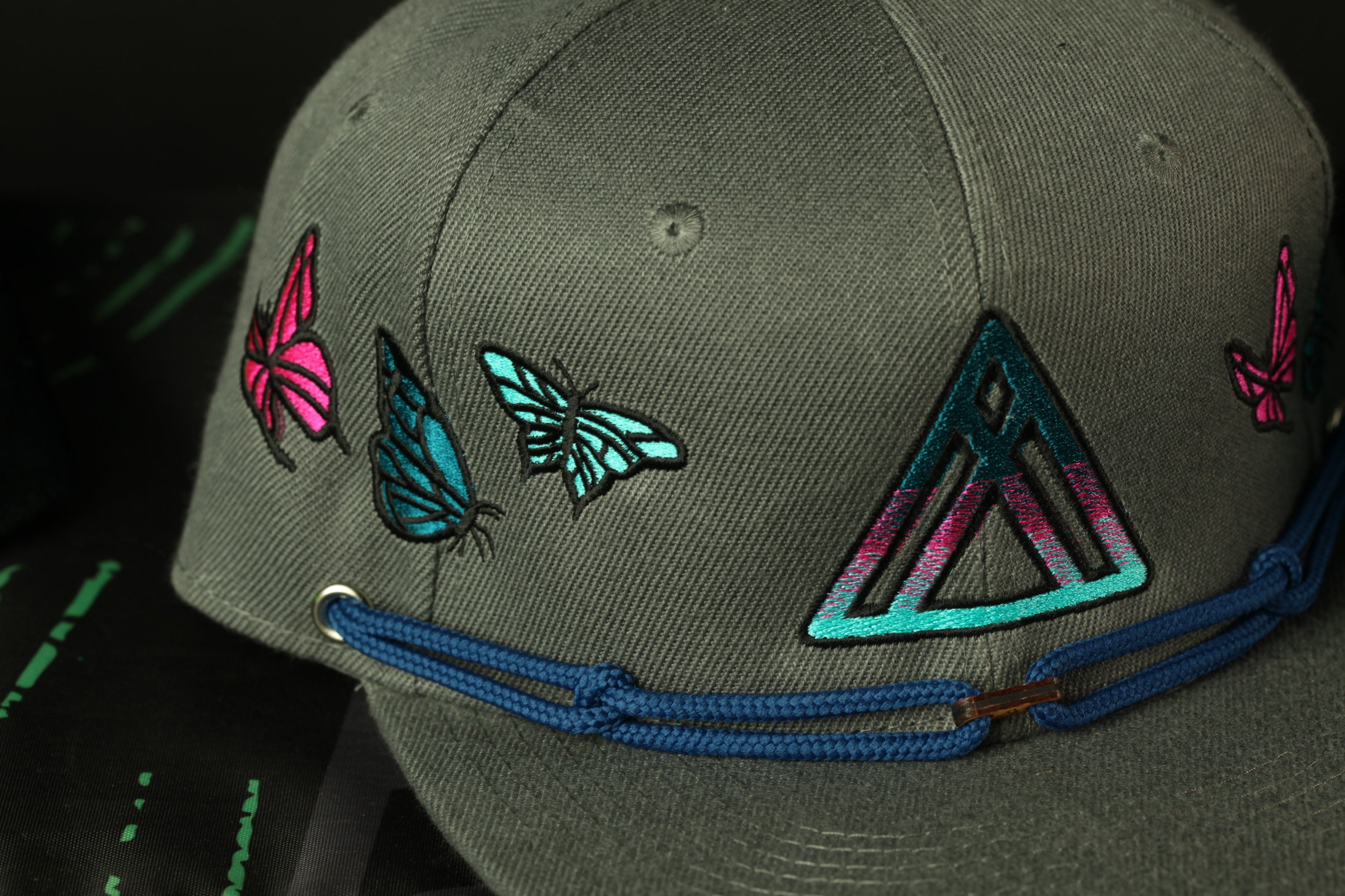 A close-up view of a gray baseball cap with colorful butterfly and geometric designs on the front.