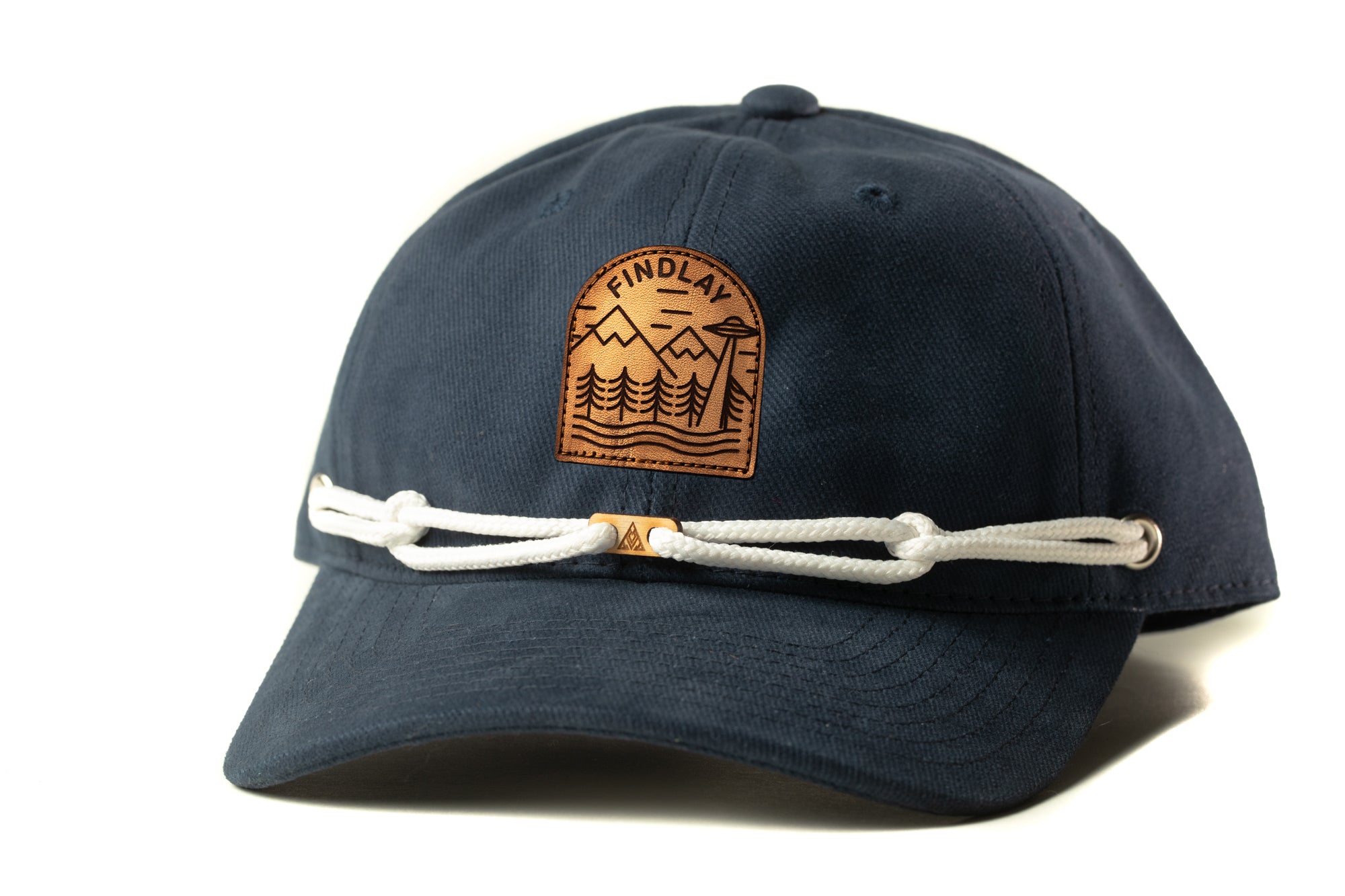 A navy blue baseball cap with a white rope and a leather patch on the front, featuring a mountain landscape design.