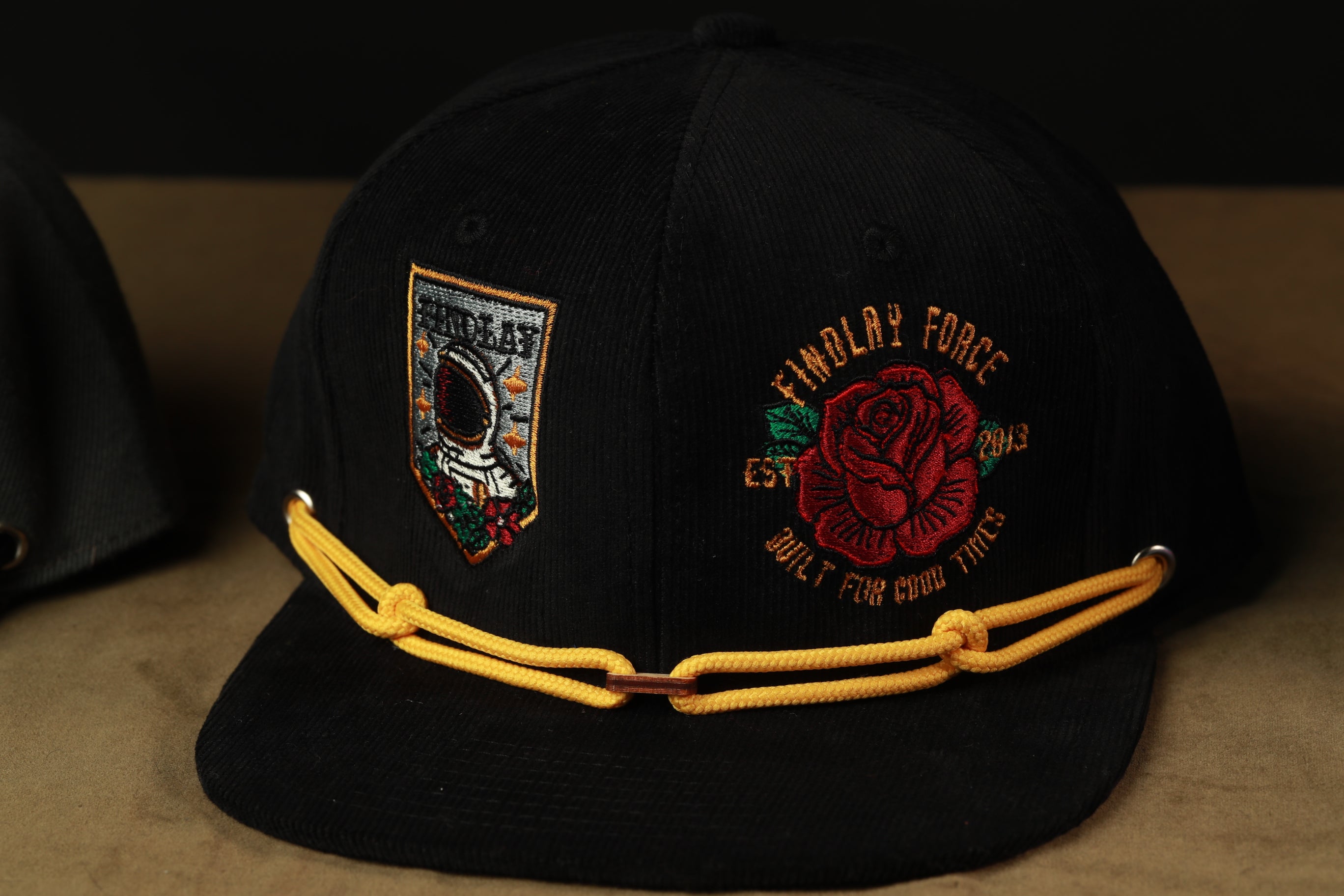 A black baseball cap with yellow strings and two patches on the front.