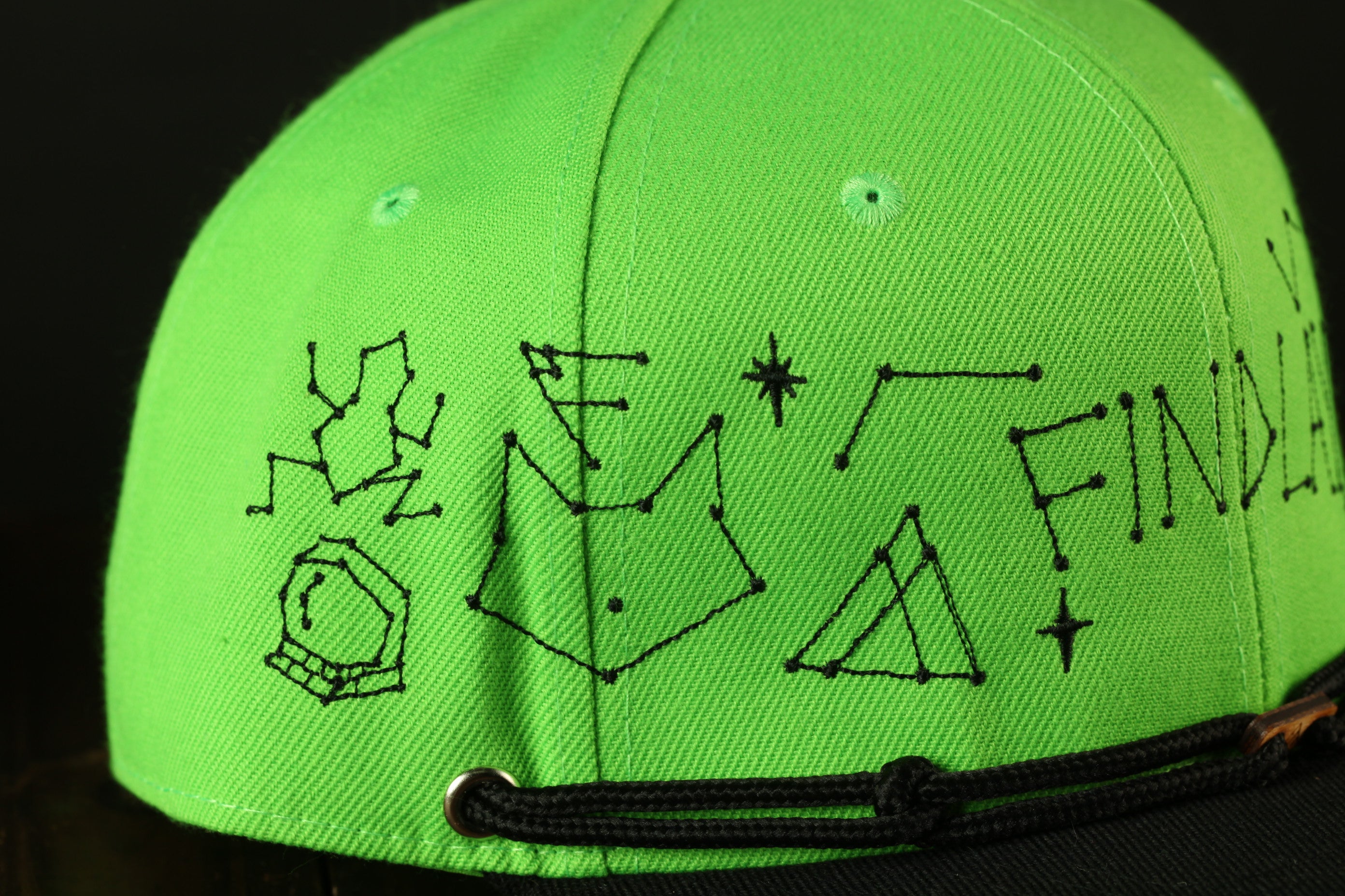 A close-up view of a bright green baseball cap with various black symbols and text embroidered on it.