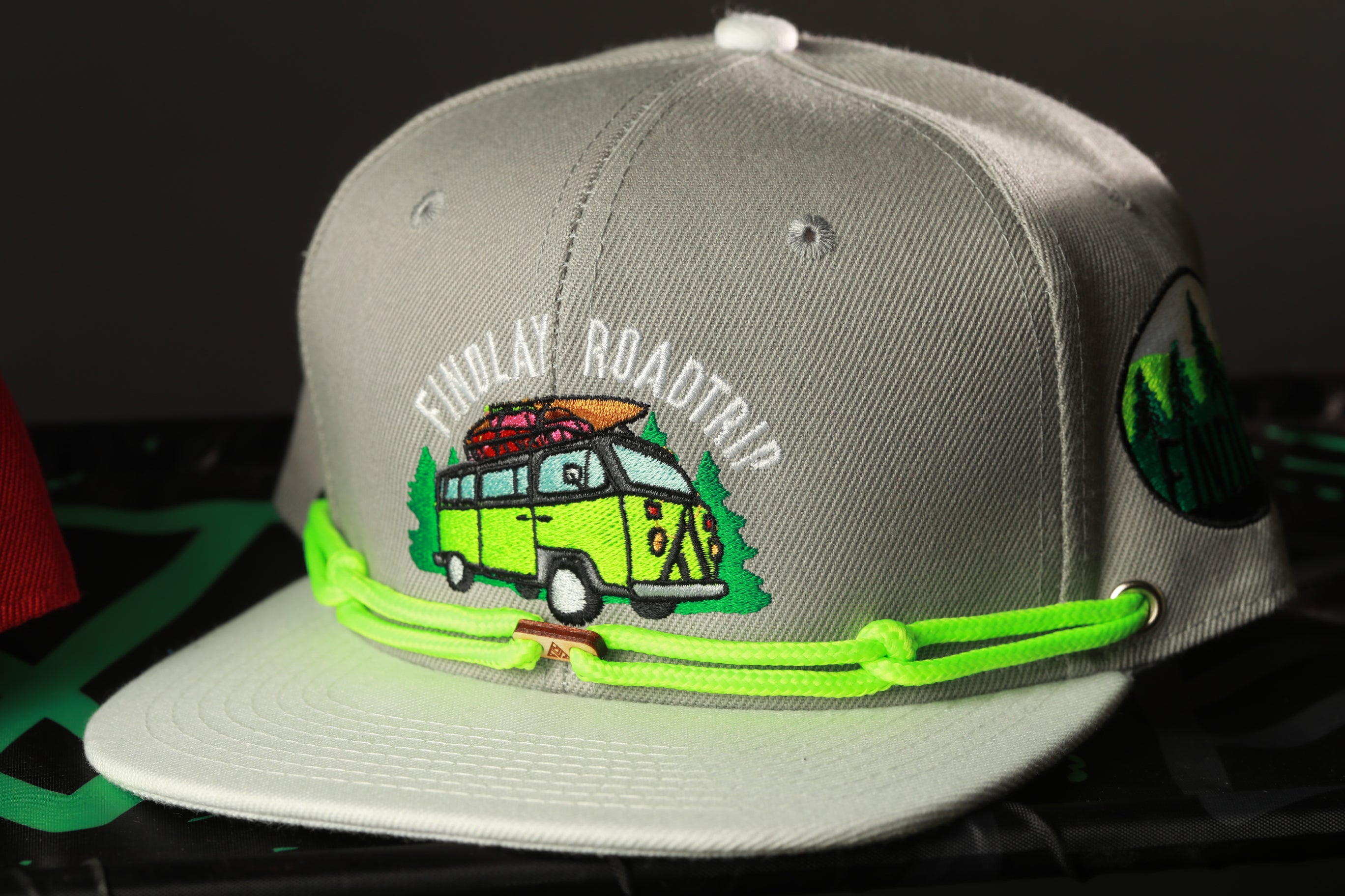 A gray baseball cap with a green and white embroidered design depicting a van and the text "Findlay Road Trip" on the front.