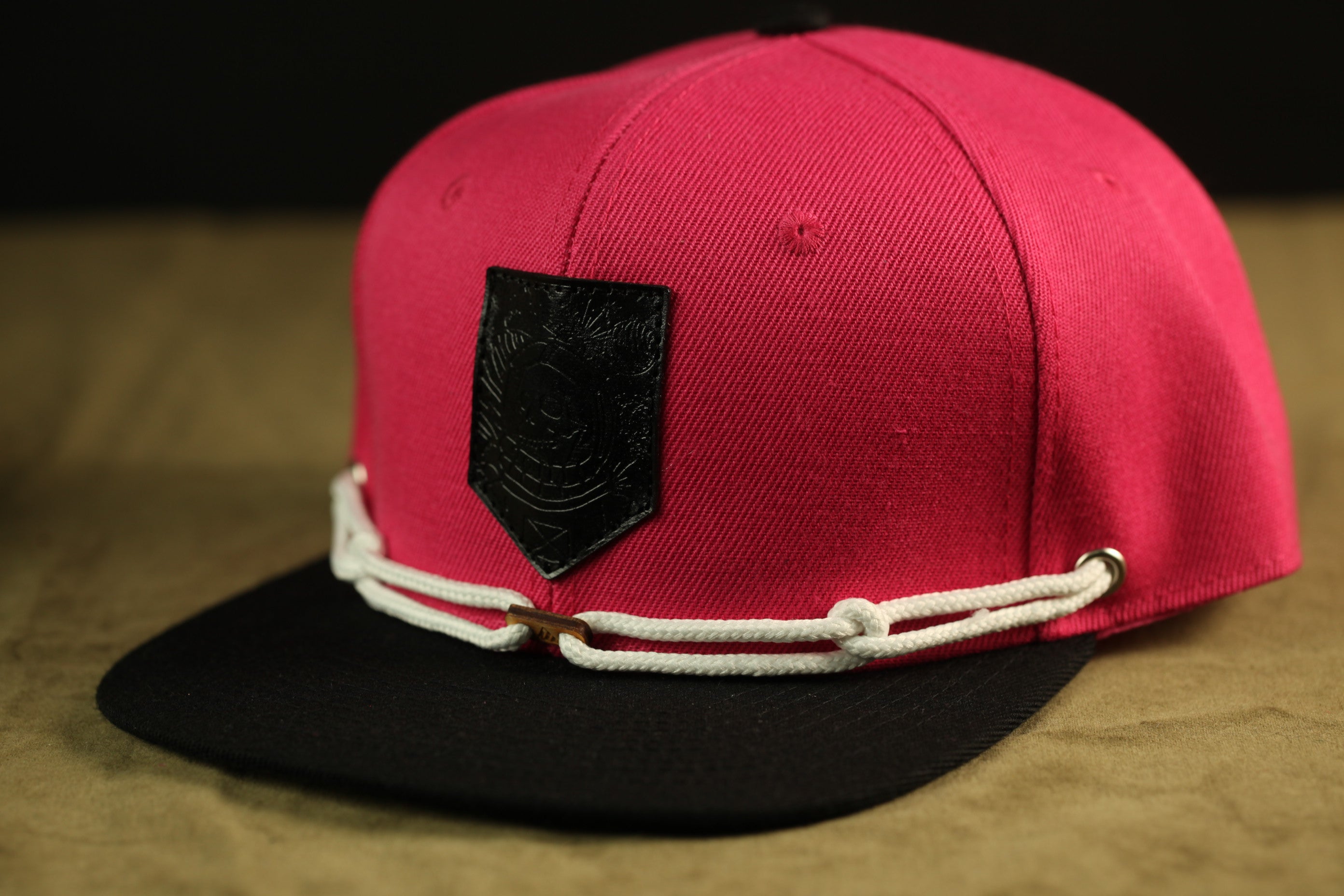 A red baseball cap with a black patch and white strings is displayed against a brown background.