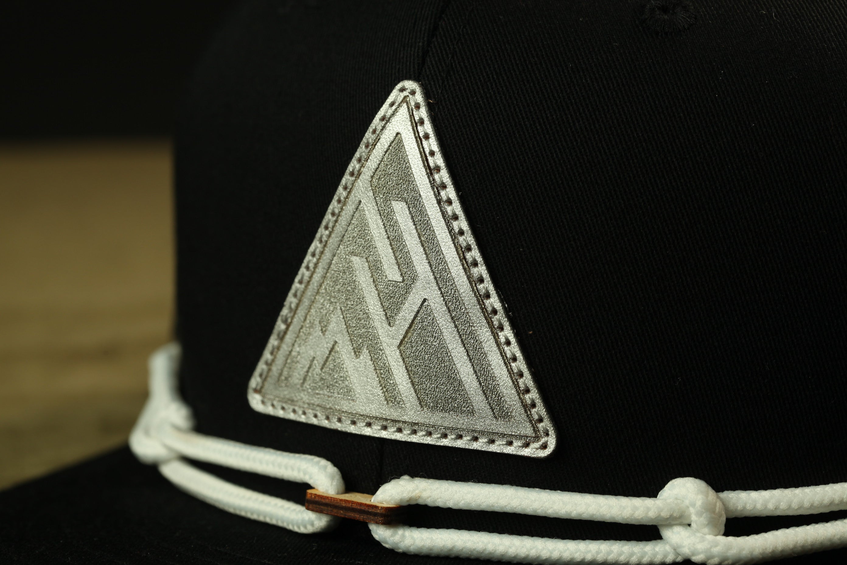 A close-up view of a black baseball cap with a white triangular logo on the front.