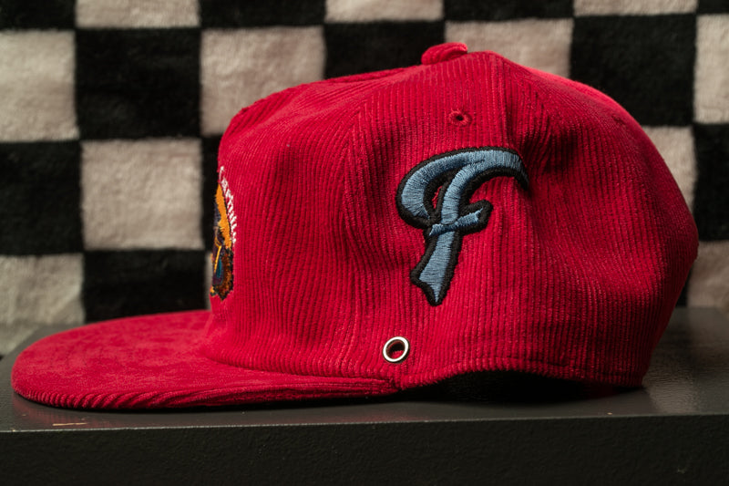 A red baseball cap with a blue "F" logo on the side, placed on a black surface against a checkered background.