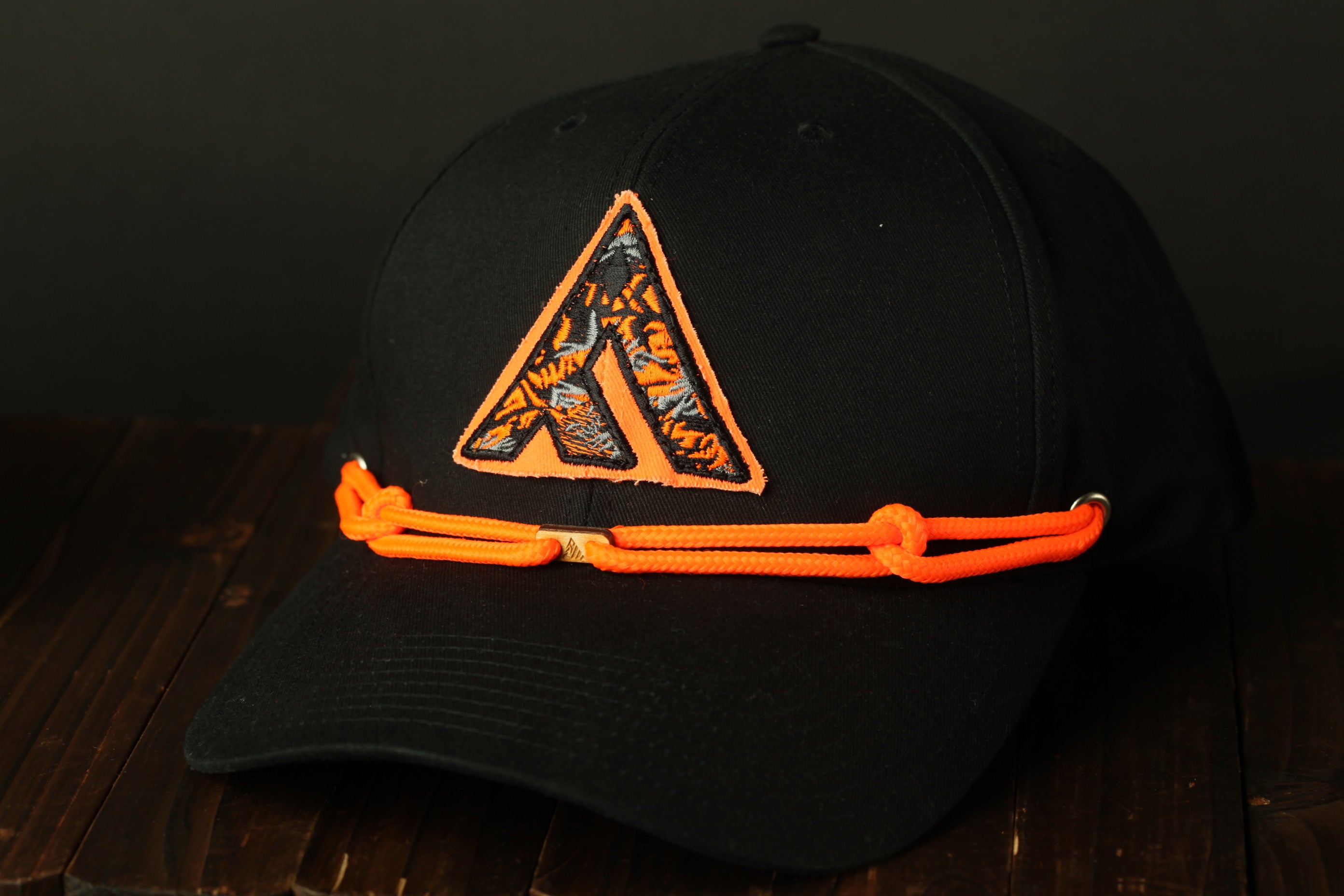 A black baseball cap with an orange and black logo on the front, sitting on a wooden surface.