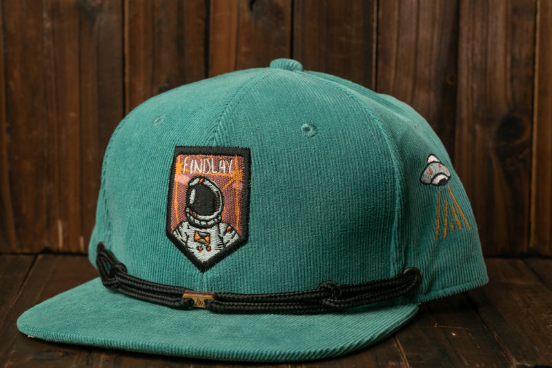 A turquoise baseball cap with a black strap and a patch featuring an astronaut.