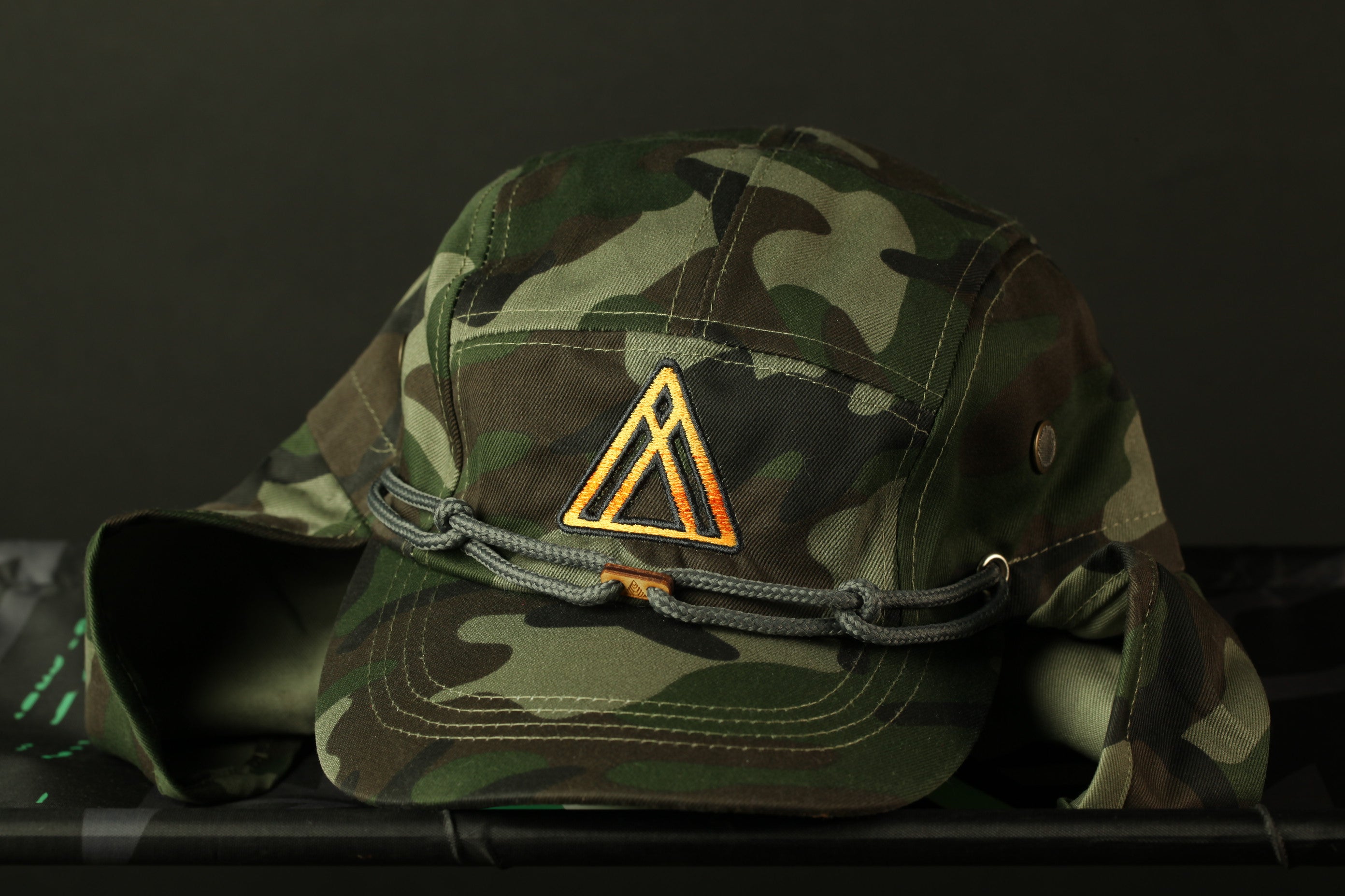 A camouflage military-style hat with a triangular emblem on the front.