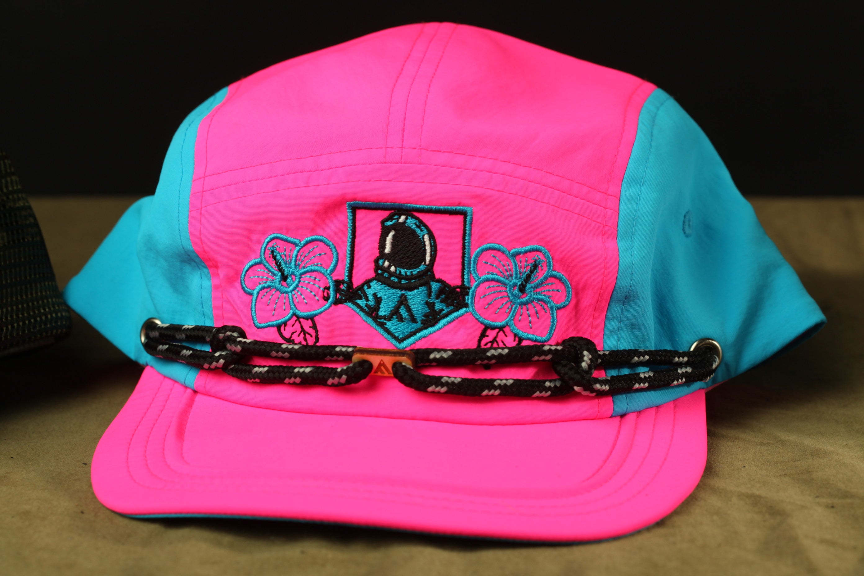 A pink and blue baseball cap with a floral design and a black strap.