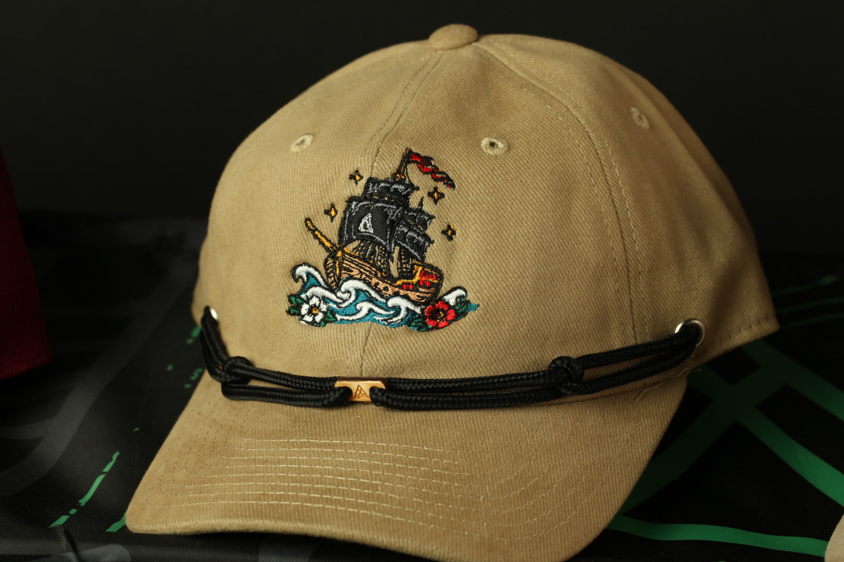A beige baseball cap with a black band and a ship embroidered on the front.
