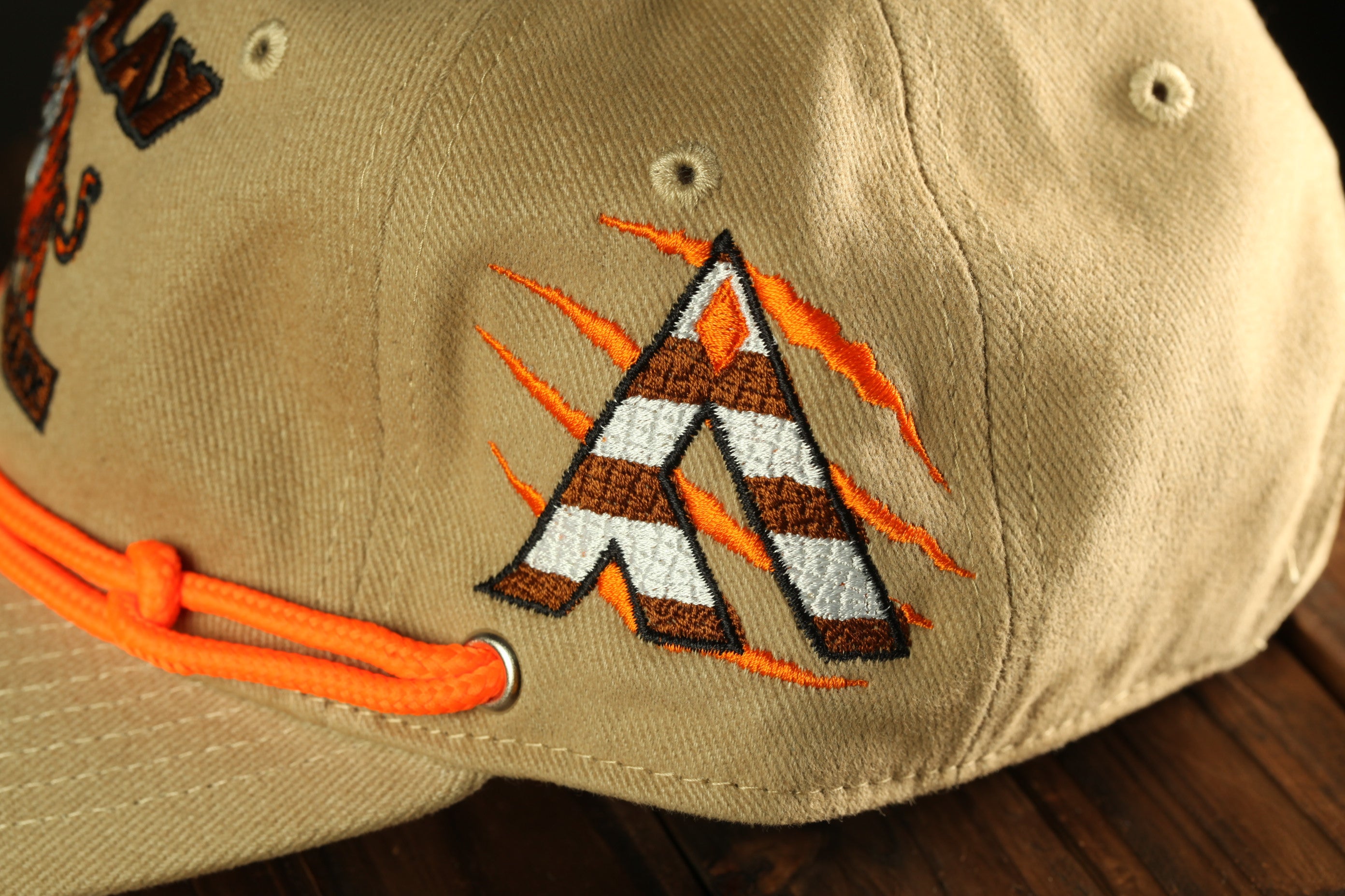 A close-up view of a beige baseball cap with a unique embroidered logo on the front.