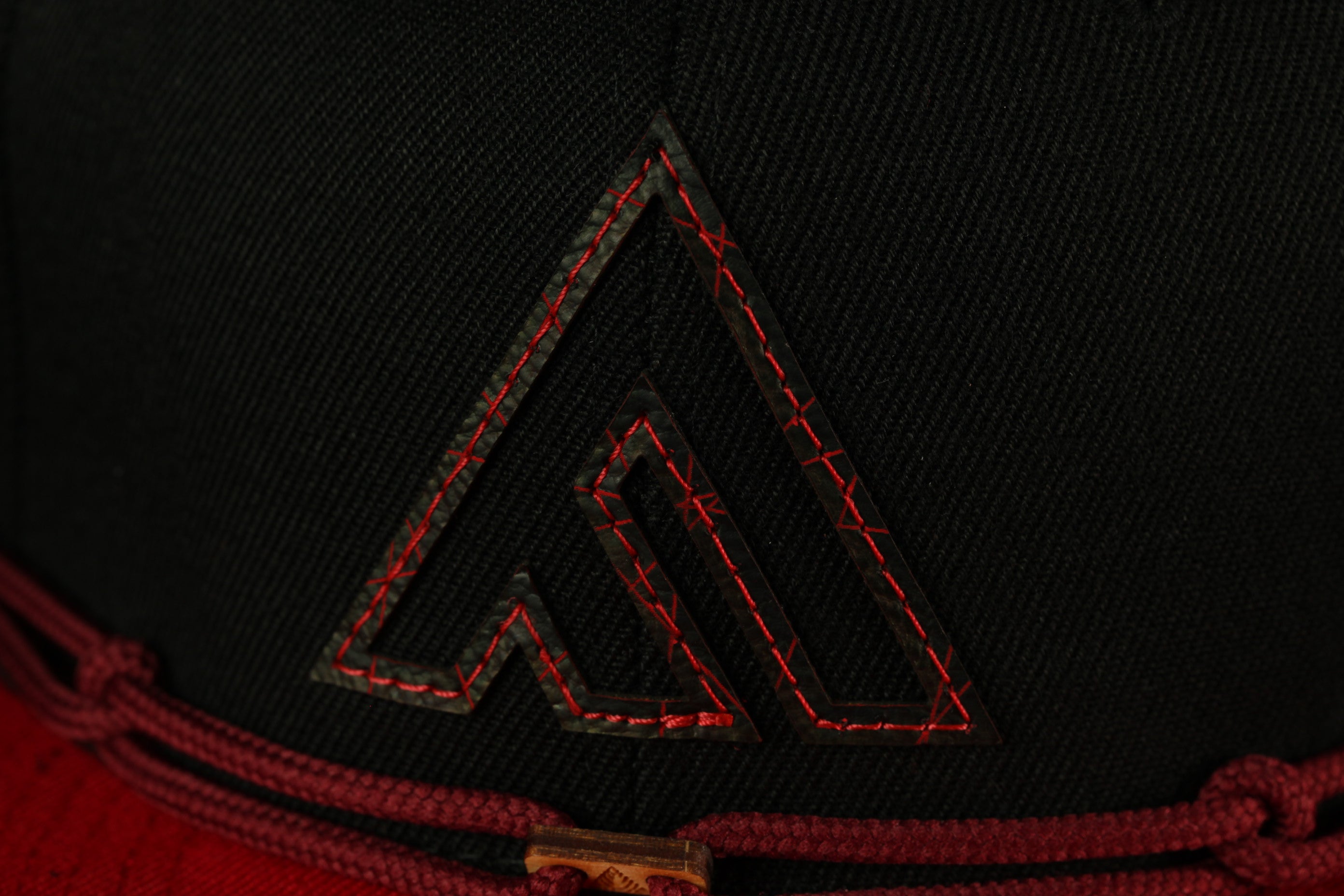 A close-up view of a black fabric with a red stitching pattern, resembling a logo or emblem.