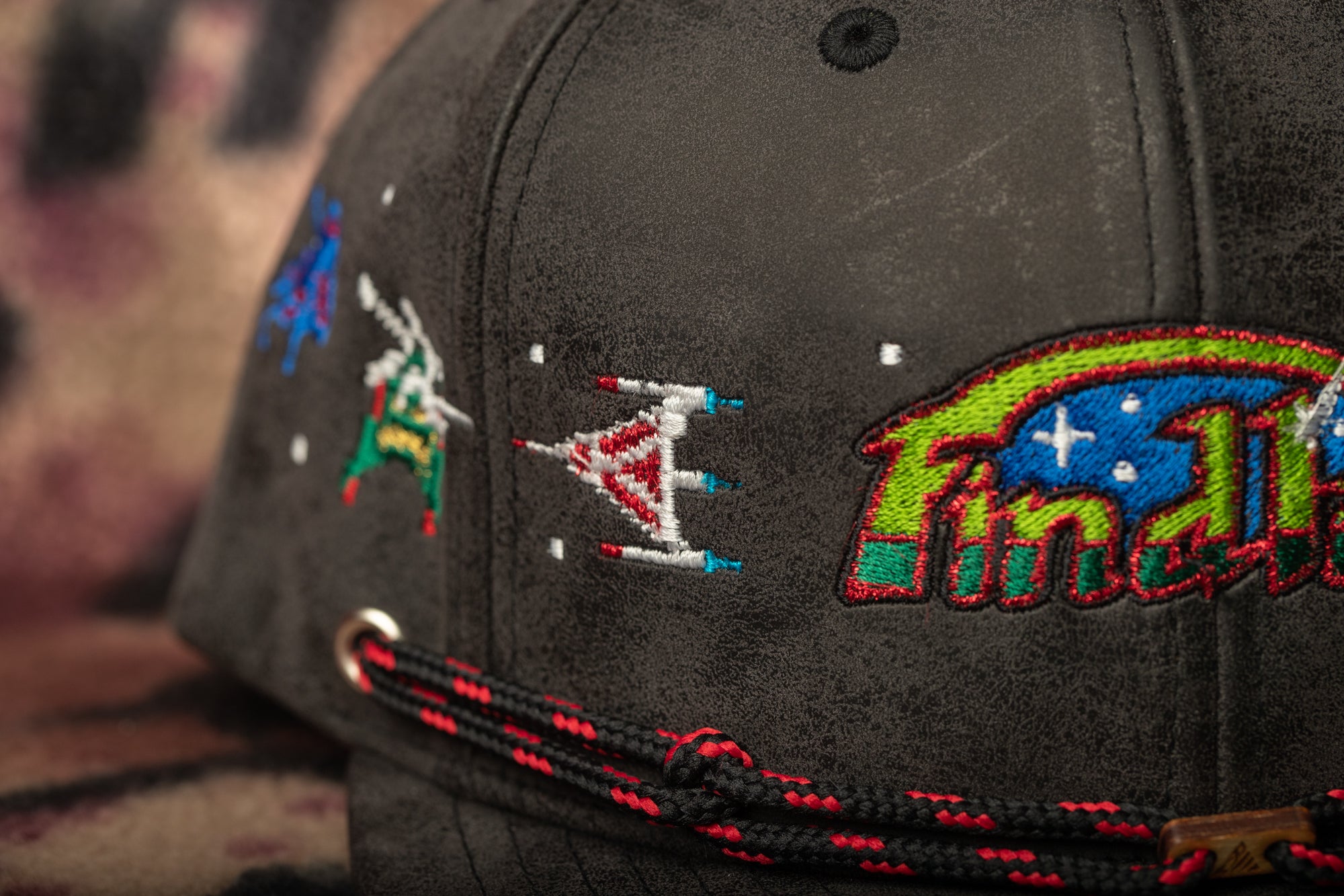 a close-up view of a black baseball cap with colorful embroidered designs on the front.