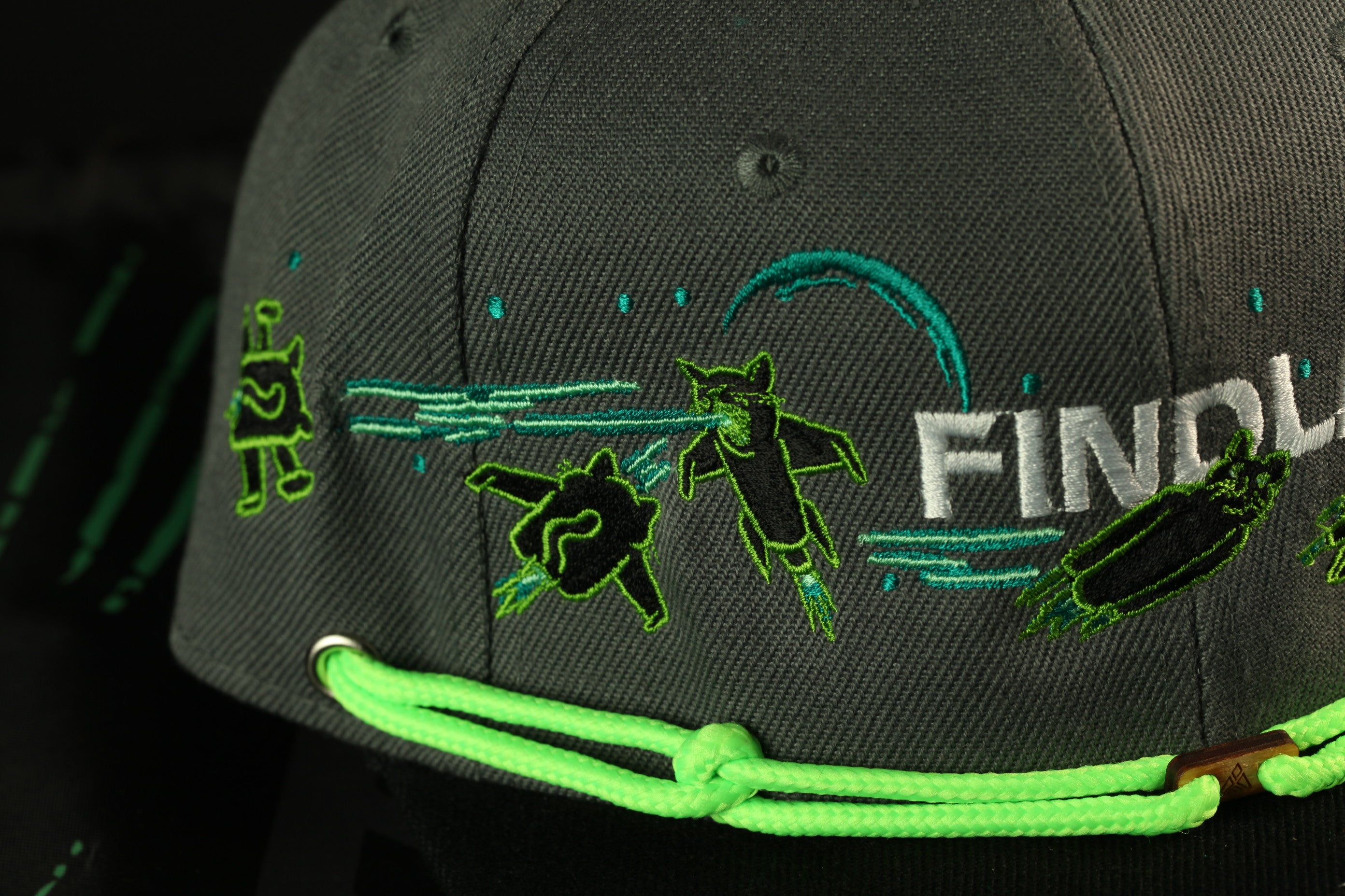 a close-up view of a gray baseball cap with various green and black embroidered designs on it.