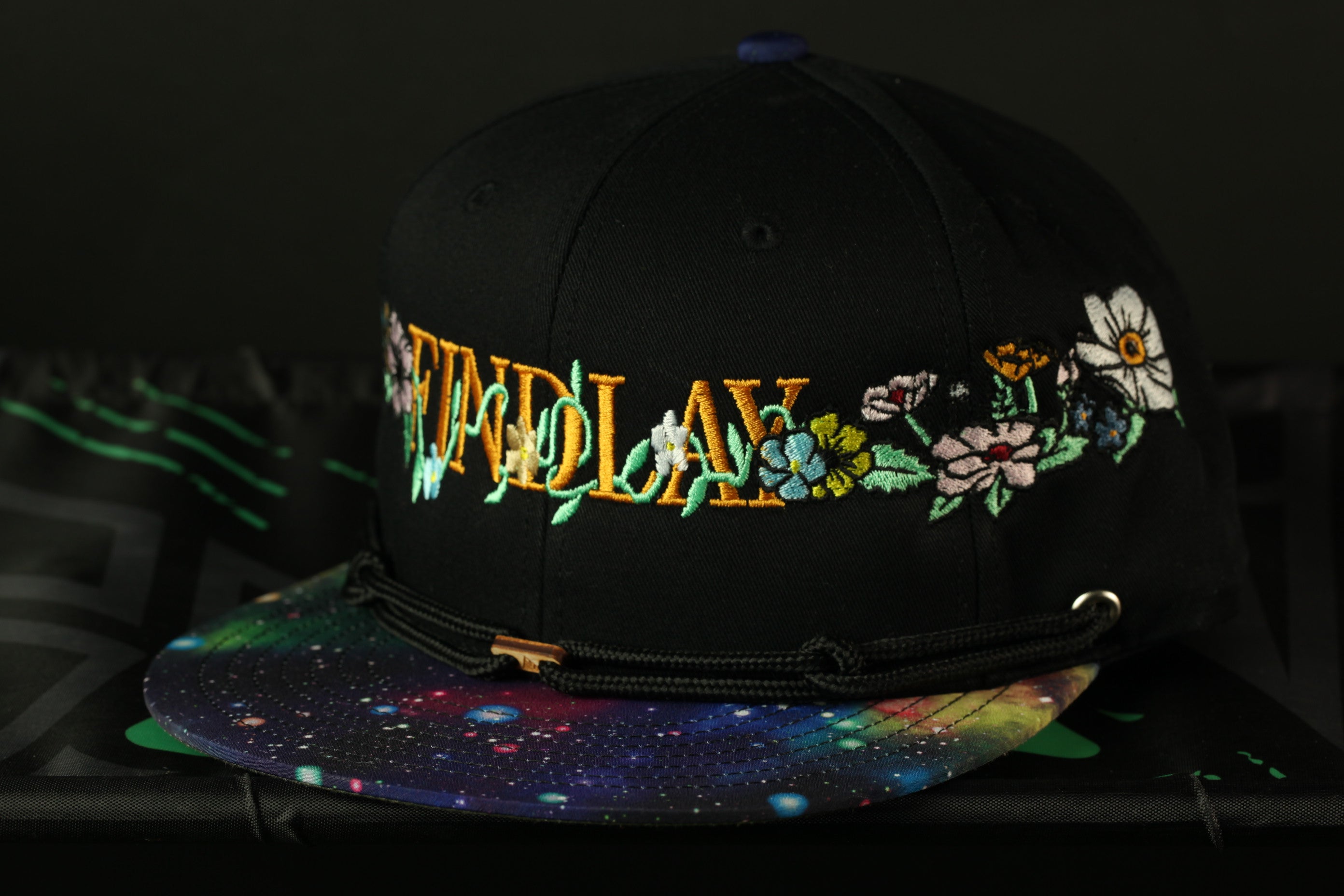 A black baseball cap with colorful floral embroidery and the word "FINDLAY" printed on it.