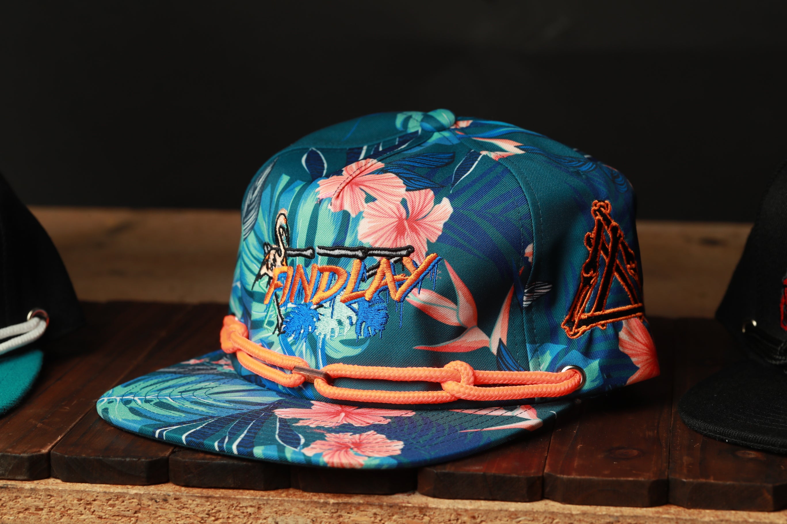 A colorful floral printed baseball cap with orange and blue accents, displayed on a wooden surface.