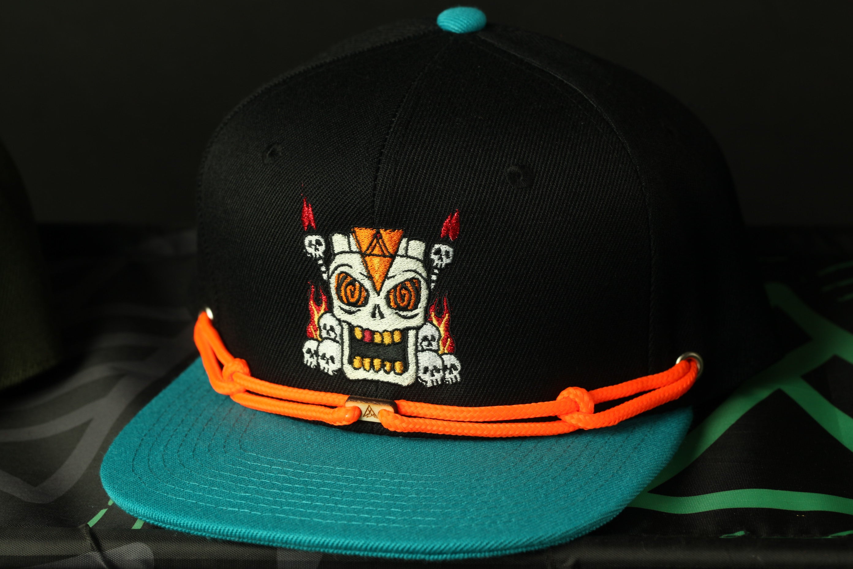 A black baseball cap with a colorful skull design and orange straps.