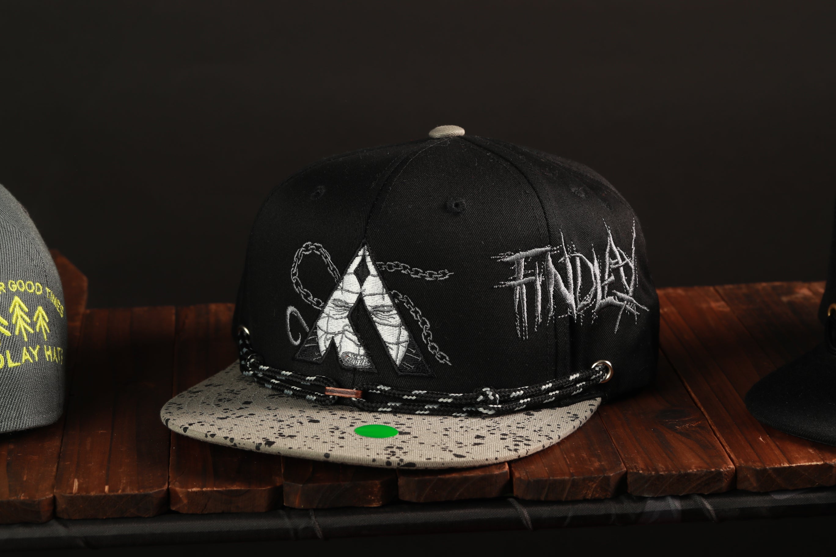 A black baseball cap with a white and gray speckled pattern, featuring a graphic design and the word "FIND" written on it.