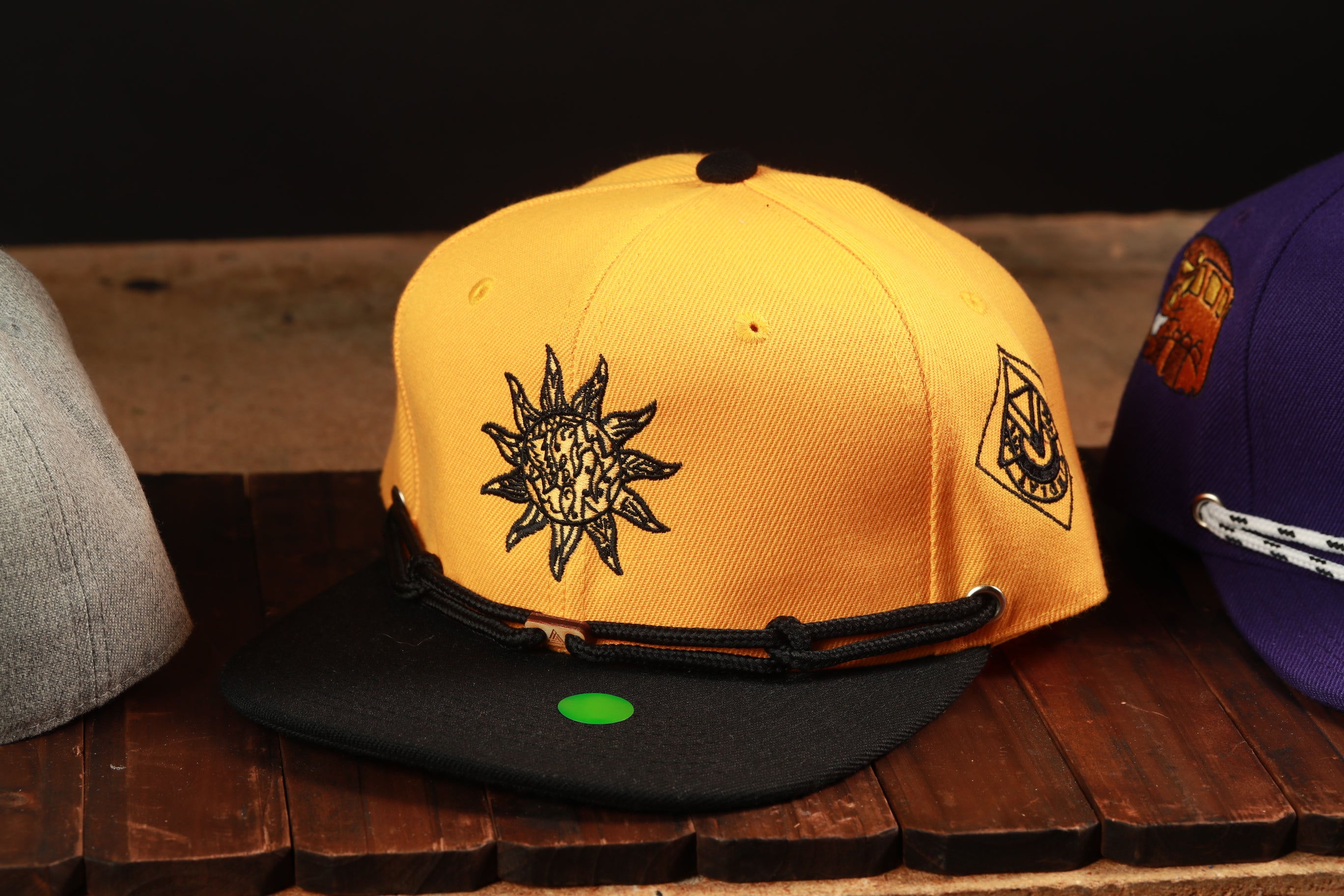 A yellow baseball cap with a sun design and a black band, sitting on a wooden surface.
