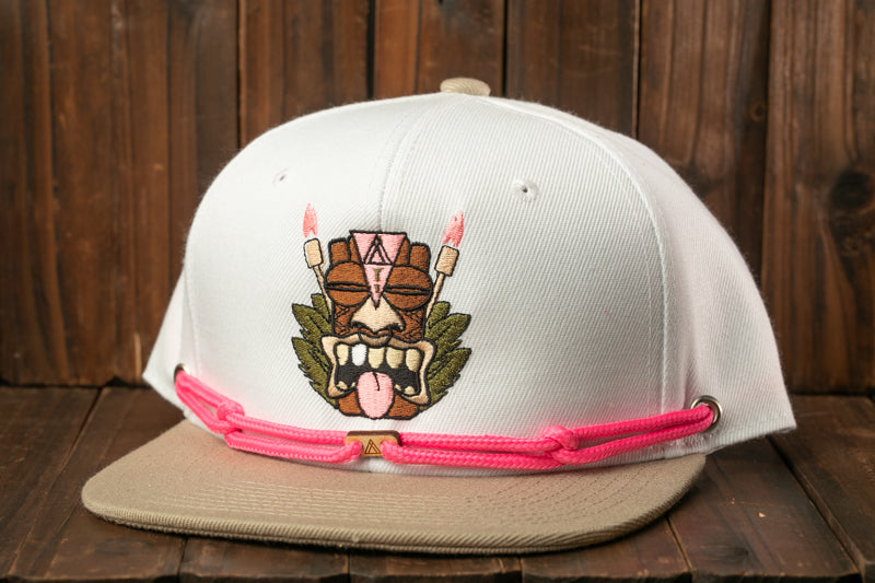 A white baseball cap with a colorful graphic design on the front, featuring a tiki mask and flames.