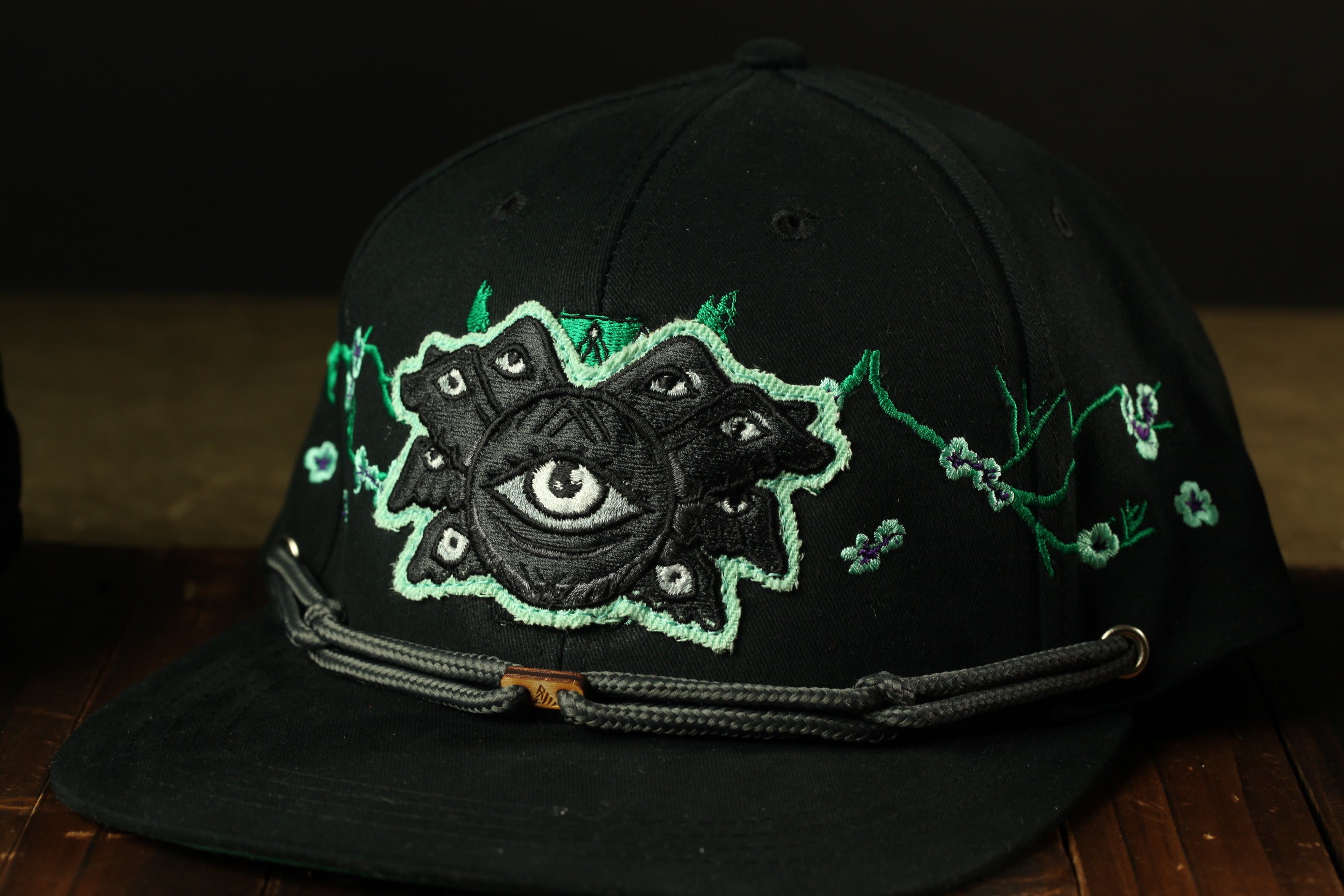 A black baseball cap with a unique eye design on the front.