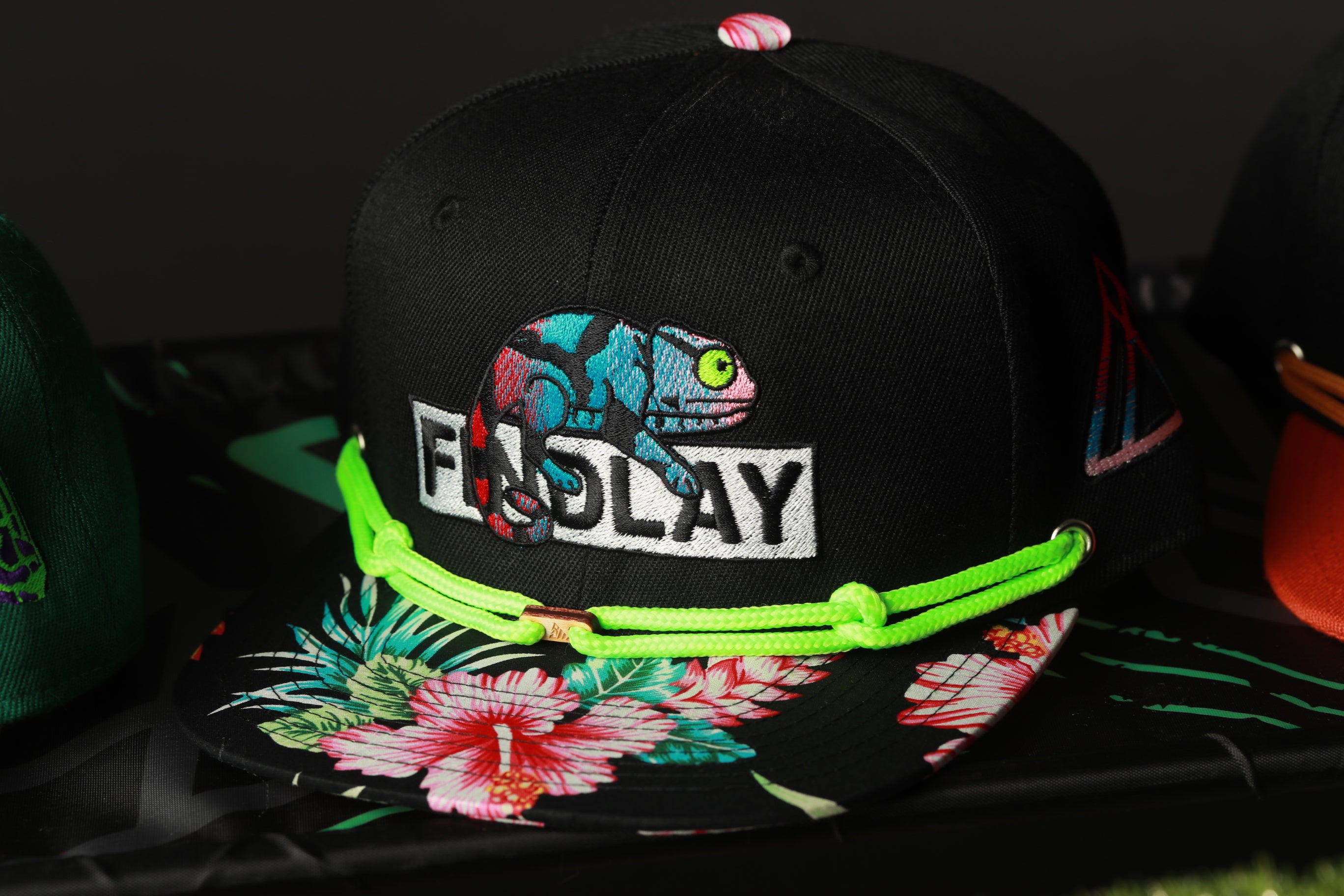 A black baseball cap with a colorful floral pattern and a chameleon design, featuring the word "FALLAY" on the front.