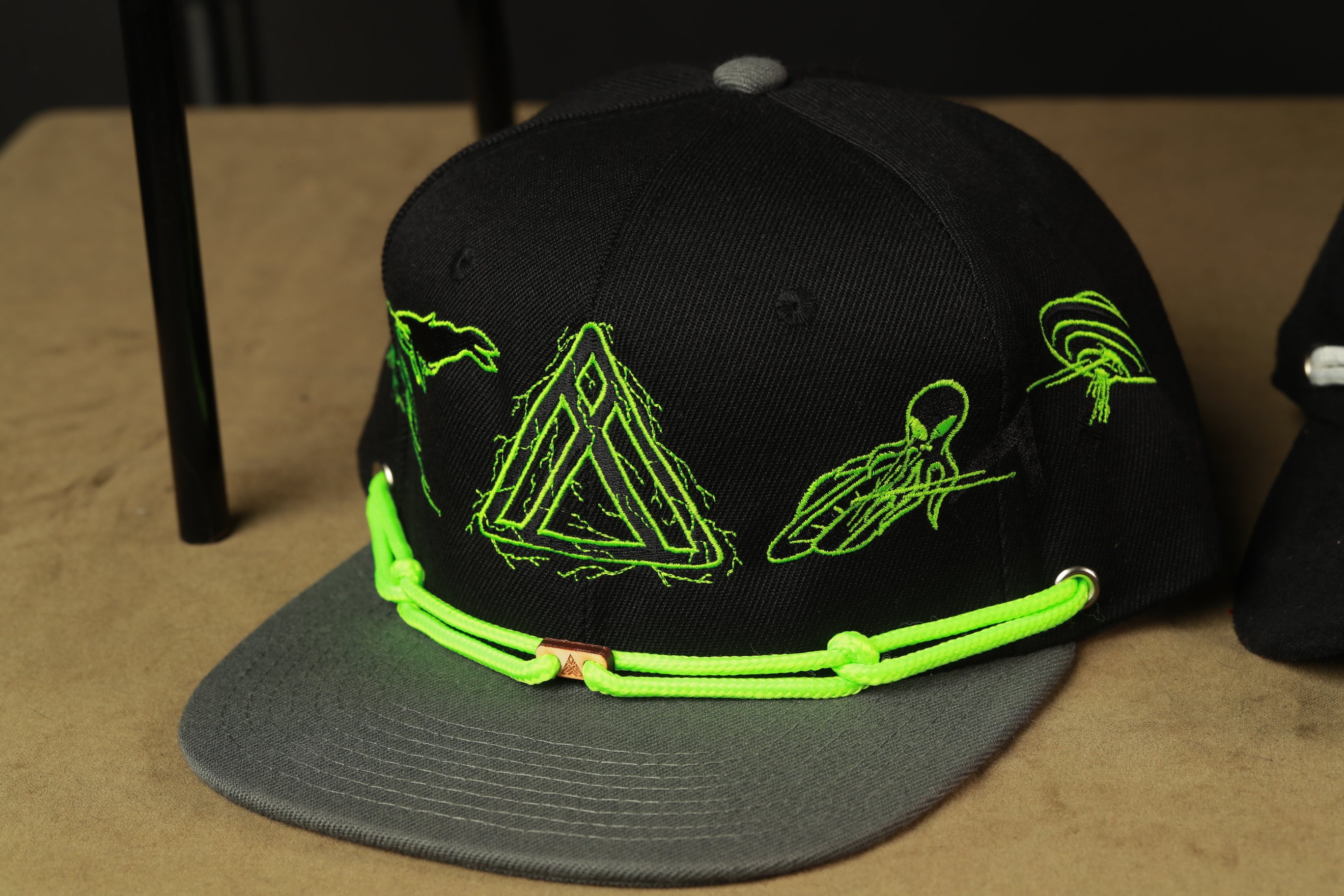 A black baseball cap with green embroidered designs on it, sitting on a table.