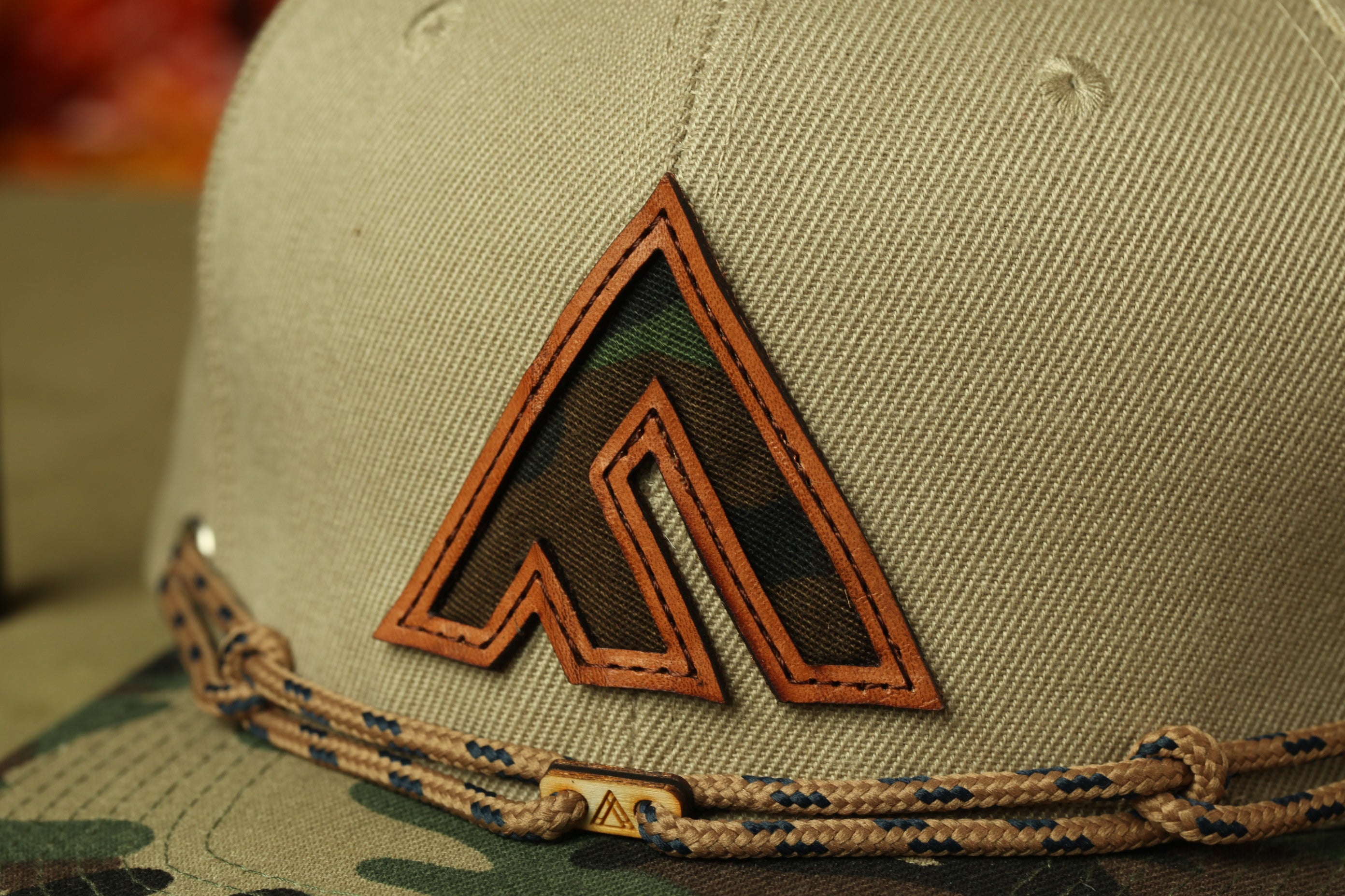 A close-up view of a beige baseball cap with a distinctive orange and green camouflage-like logo on the front.