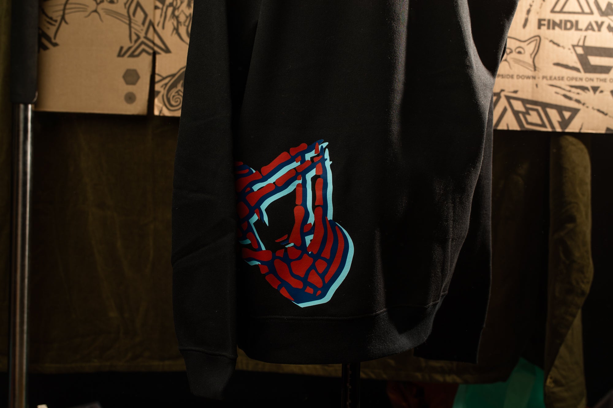 A black hoodie with a Spiderman logo printed on it, hanging on a hanger.