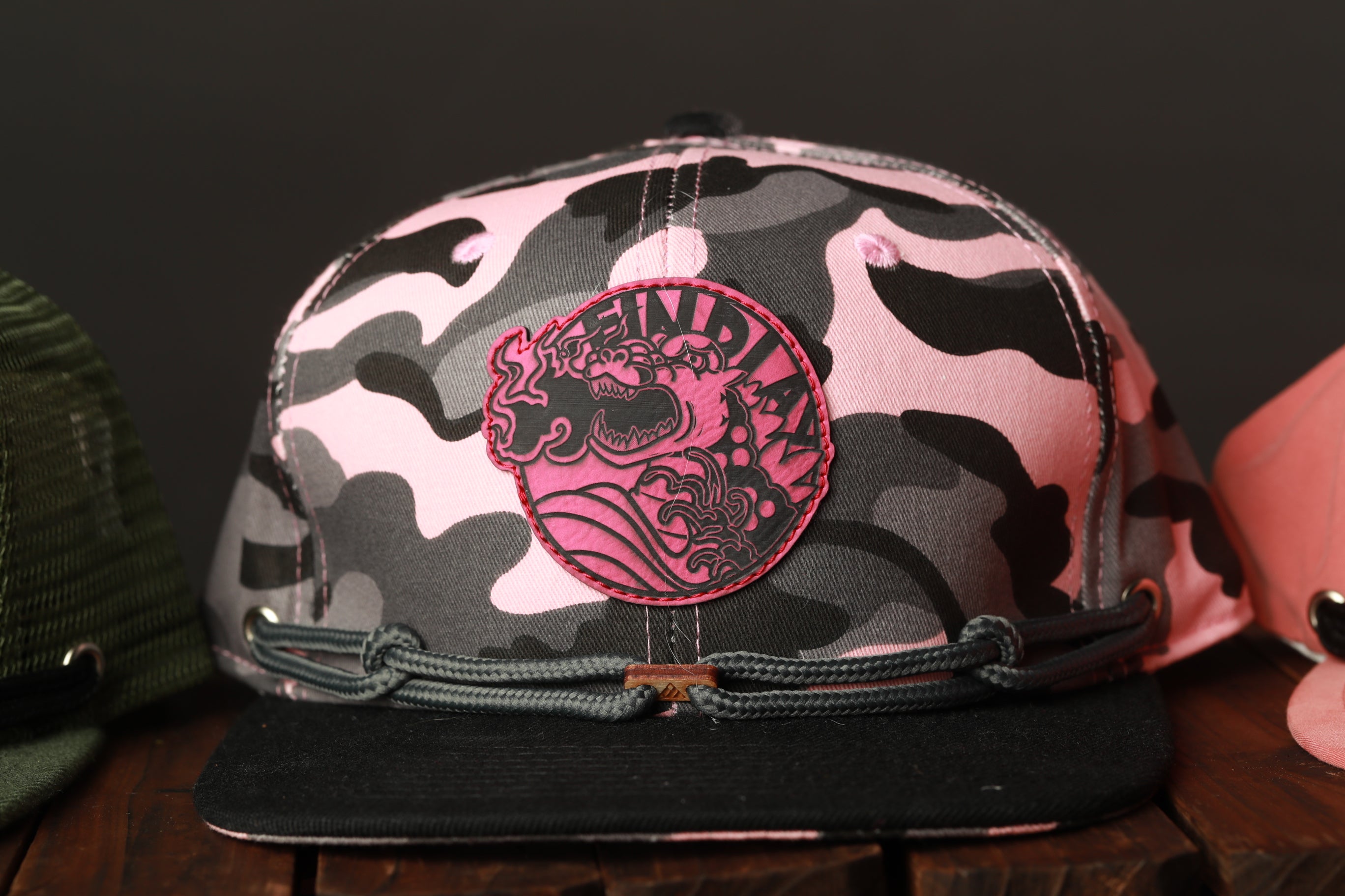 A pink and black camouflage baseball cap with a circular patch featuring a dragon design.