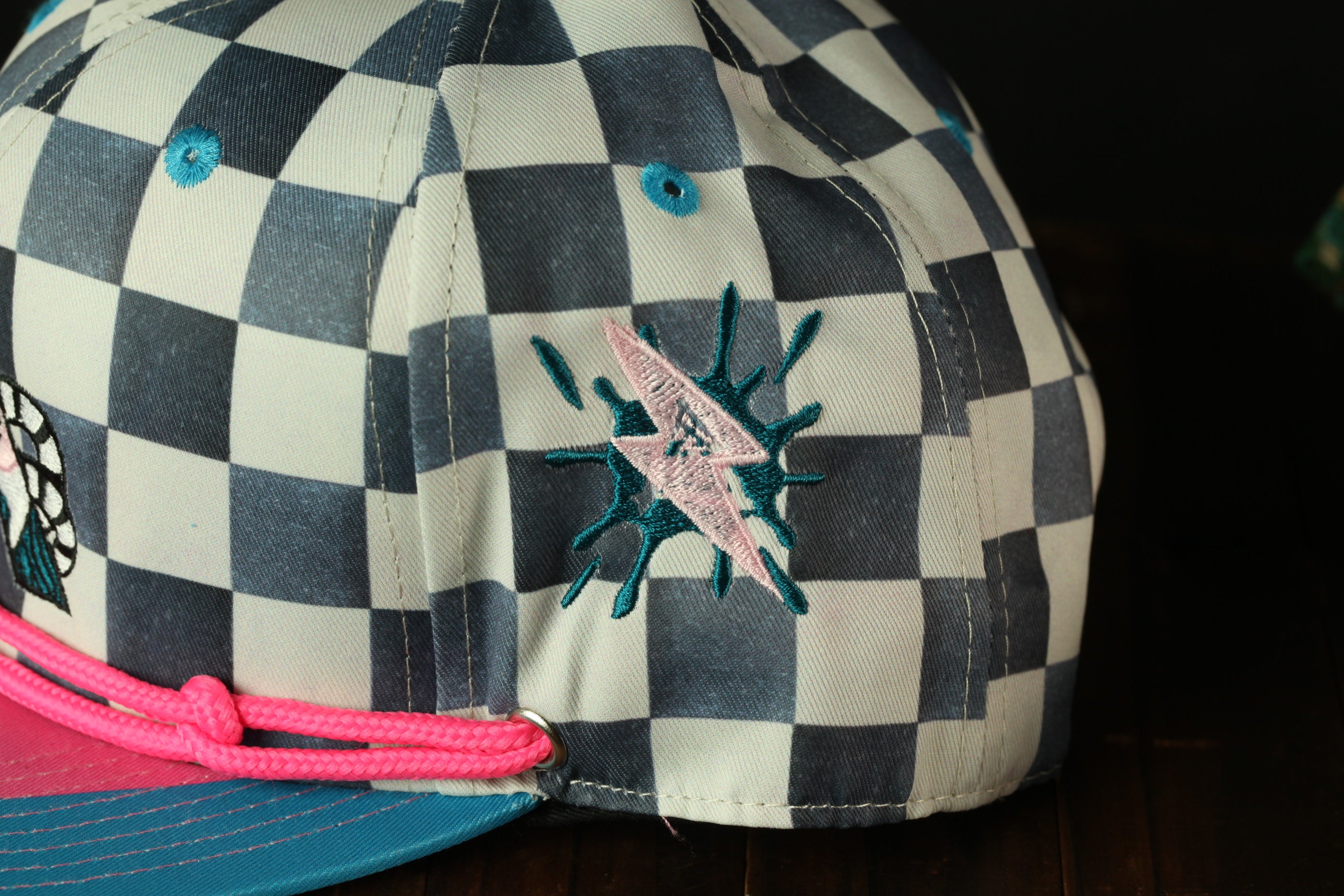 A close-up view of a baseball cap with a checkered pattern and a pink string.