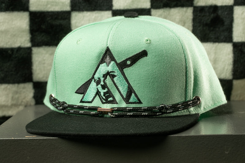 A mint green baseball cap with a black and white graphic design on the front.
