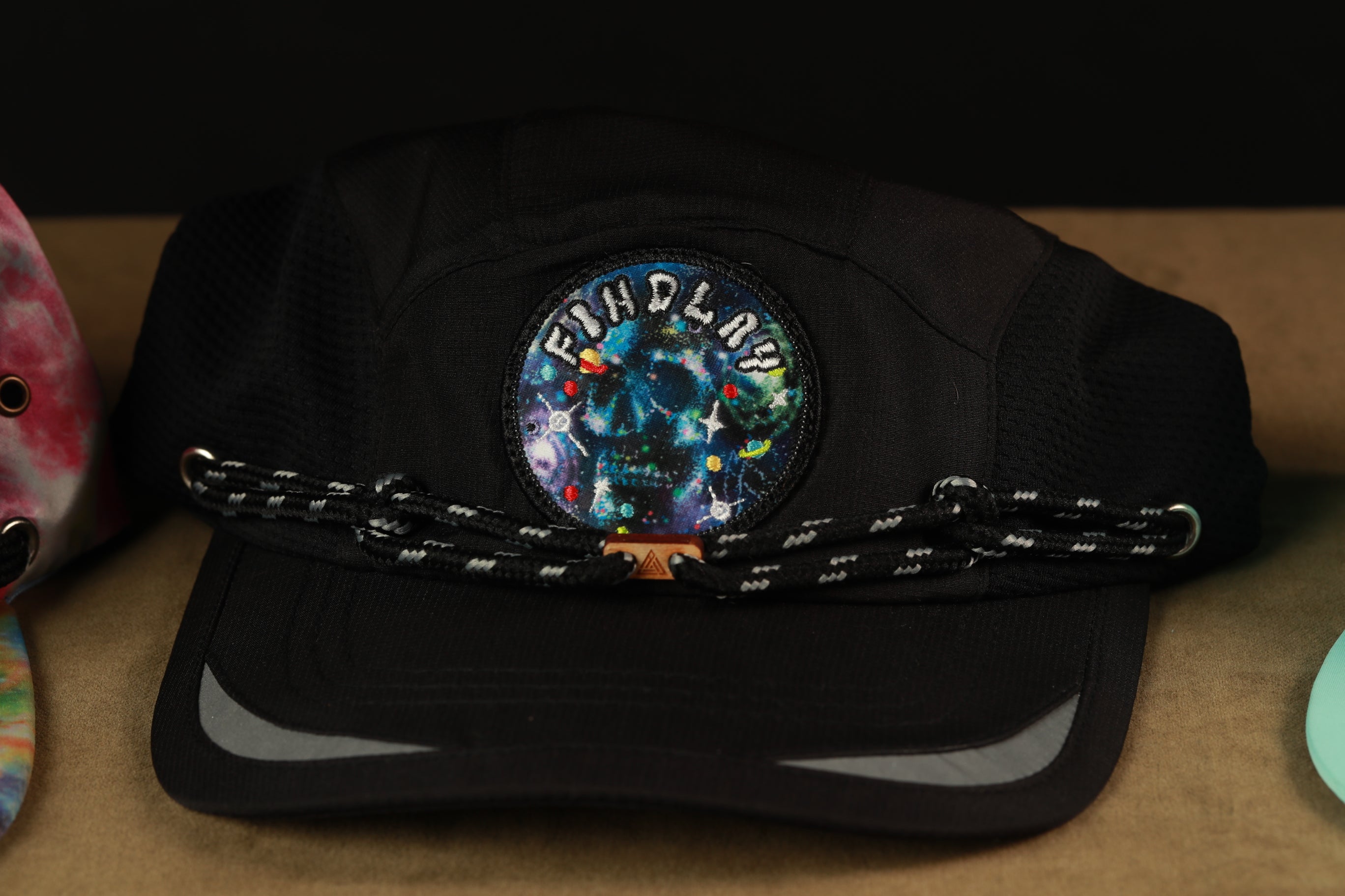 A black baseball cap with a colorful skull patch and a chain strap, placed on a surface.
