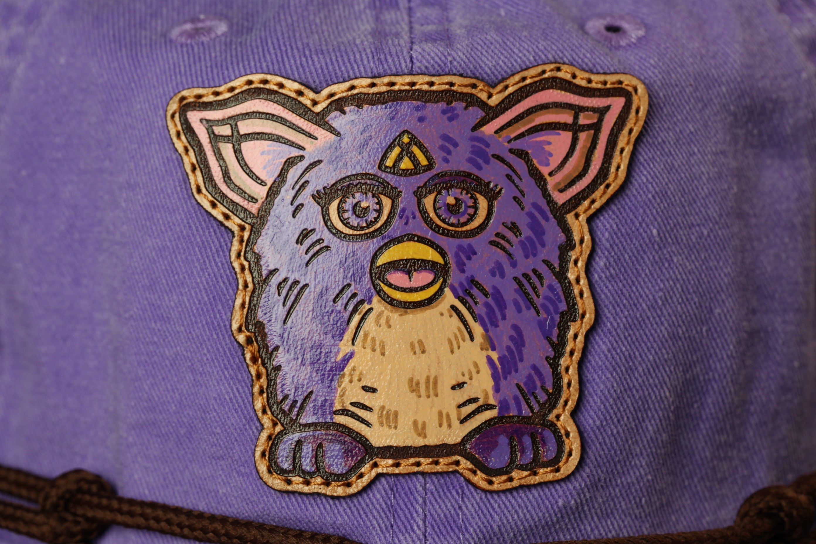 A close-up image of a purple and yellow plush toy with large eyes and a triangular head, resembling a fuzzy or plush animal.