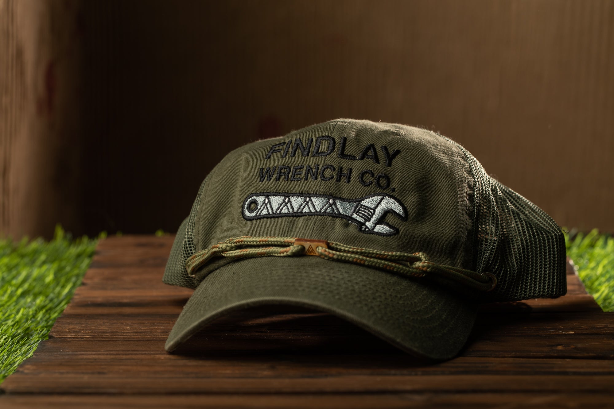 A green baseball cap with the text "Findlay Wrench Co." printed on it, sitting on a wooden surface.