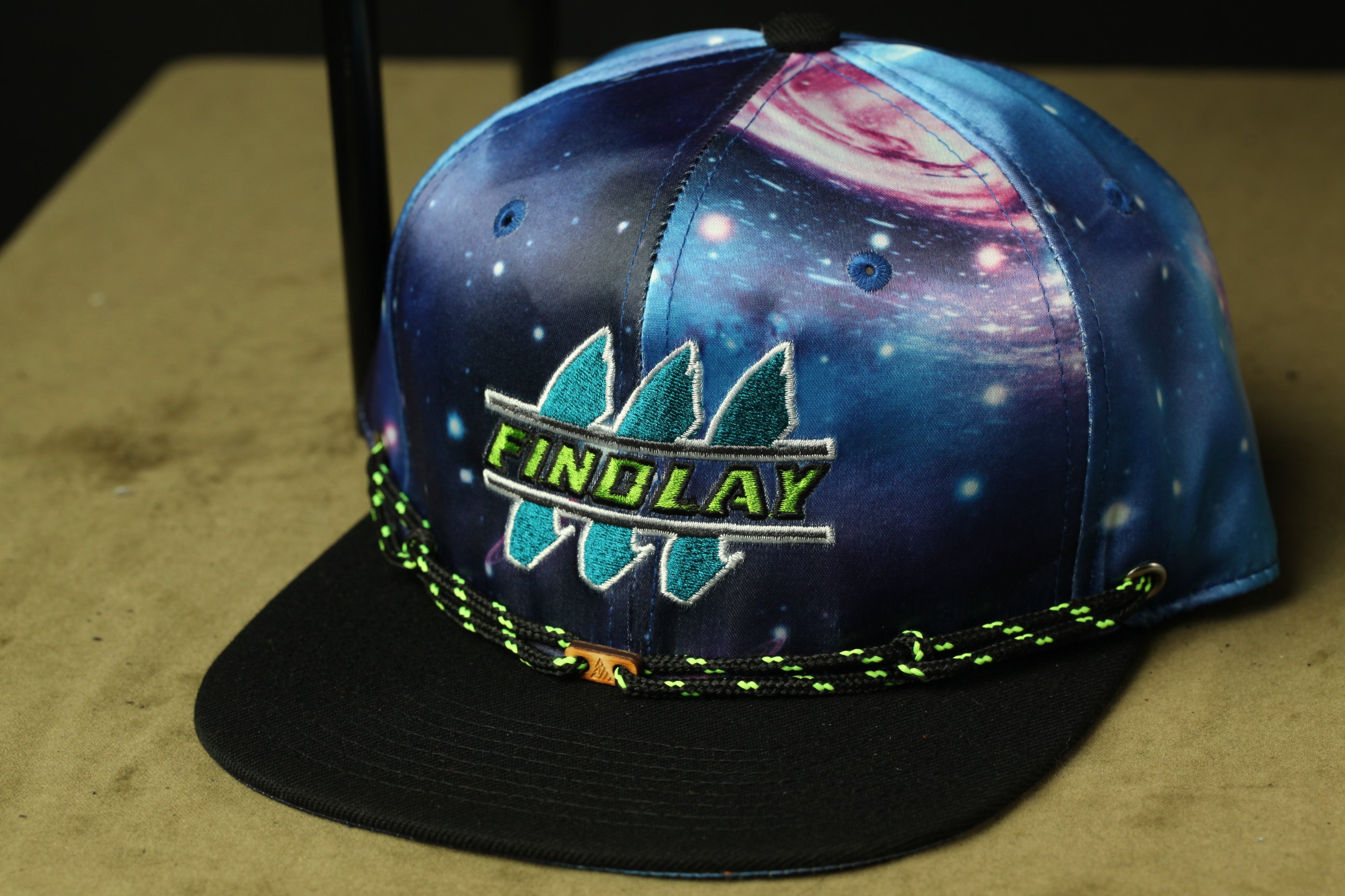 A colorful baseball cap with a space-themed design, featuring a galaxy pattern and the word "FINDlay" printed on it.