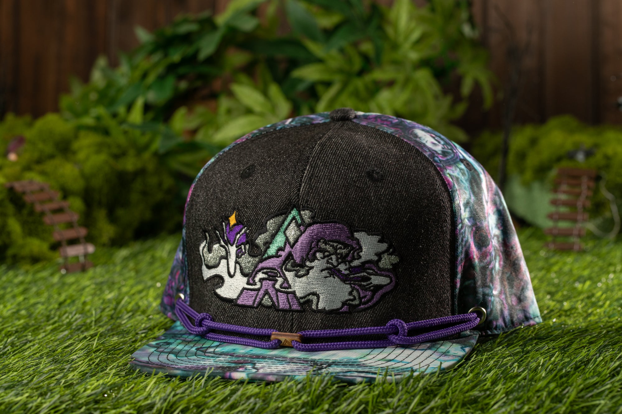 A colorful, patterned baseball cap with a dragon design sits on a grassy surface, surrounded by lush greenery.