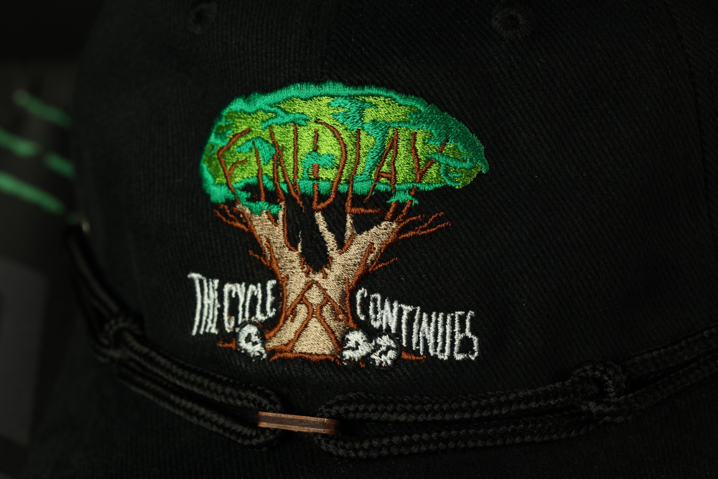 a close-up view of a black baseball cap with a tree design and text embroidered on it.